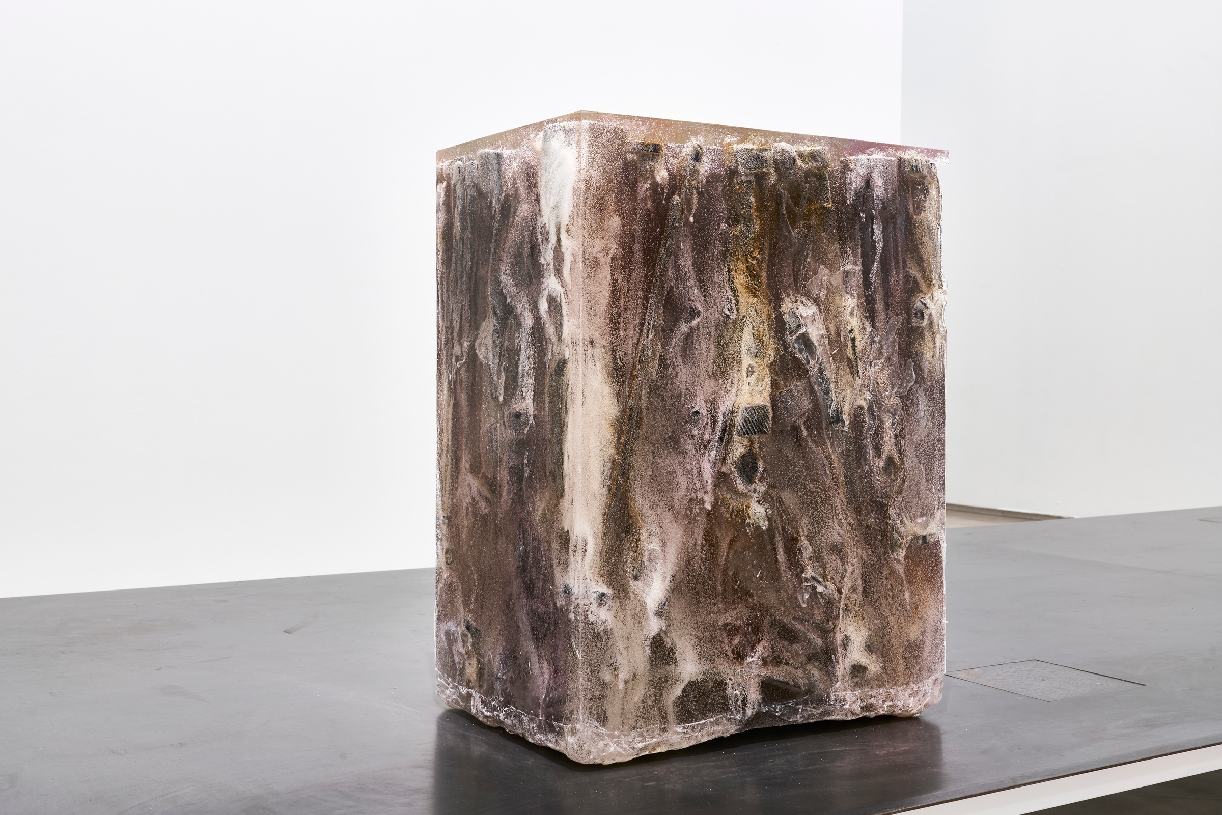 A photograph of Kevin Beasley's untitled hand-carved ebony figurine, crystal and clear resin sculpture sitting on a metal platform.
