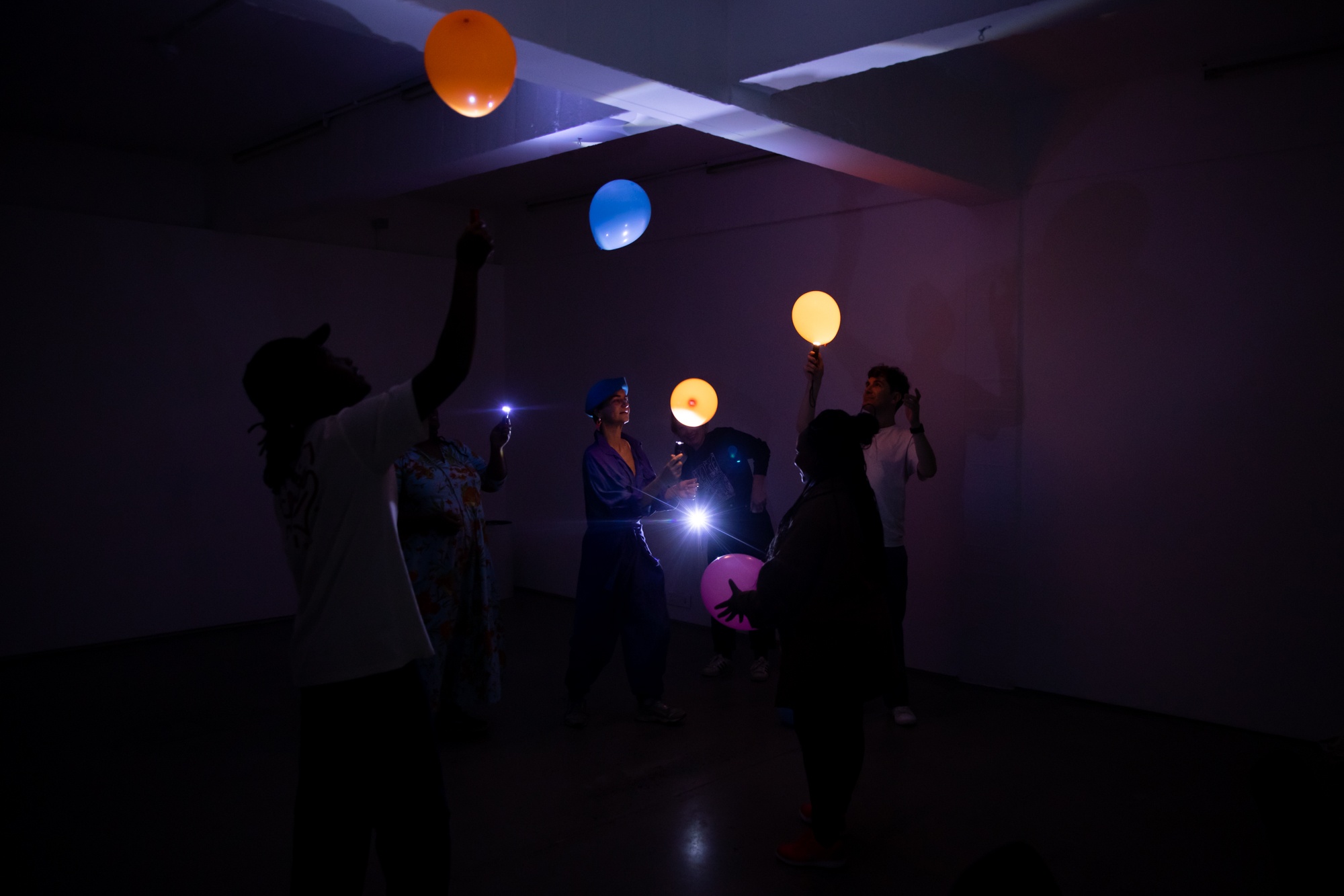 Photograph from ‘Play-Play,’ Francesco Nassimbeni's residency in the A4 Reading Room. Participants in a darkened room play at keeping balloons airborne with handheld torches.
