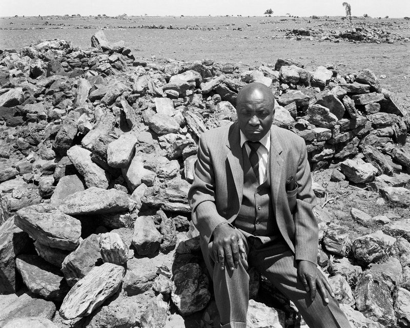 David Goldblatt's monochrome photograph 'Luke Kgatitsoe in his house, bulldozed in February 1984 by the government after the forced removal of the people of Magopa, a black-owned farm, which had been declared a "black spot", Ventersdorp district, Transvaal' shows an individual wearing a suit seated amongst rubble.
