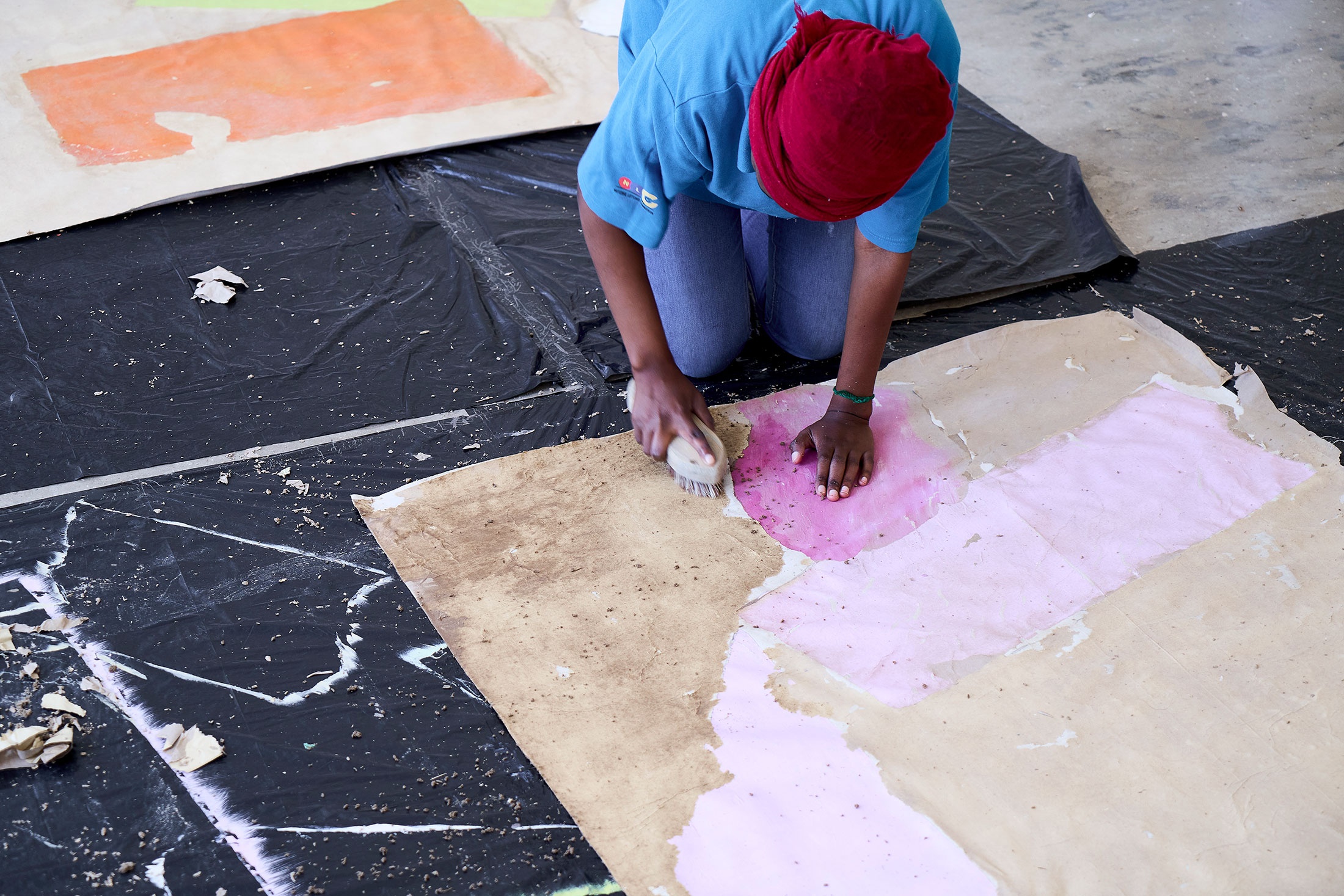 Process photograph from the 2nd rendition of ‘Parallel Play’ in A4’s Gallery. Asemahle Nltonti’s studio assistant applies paint onto brown paper on the gallery floor.
