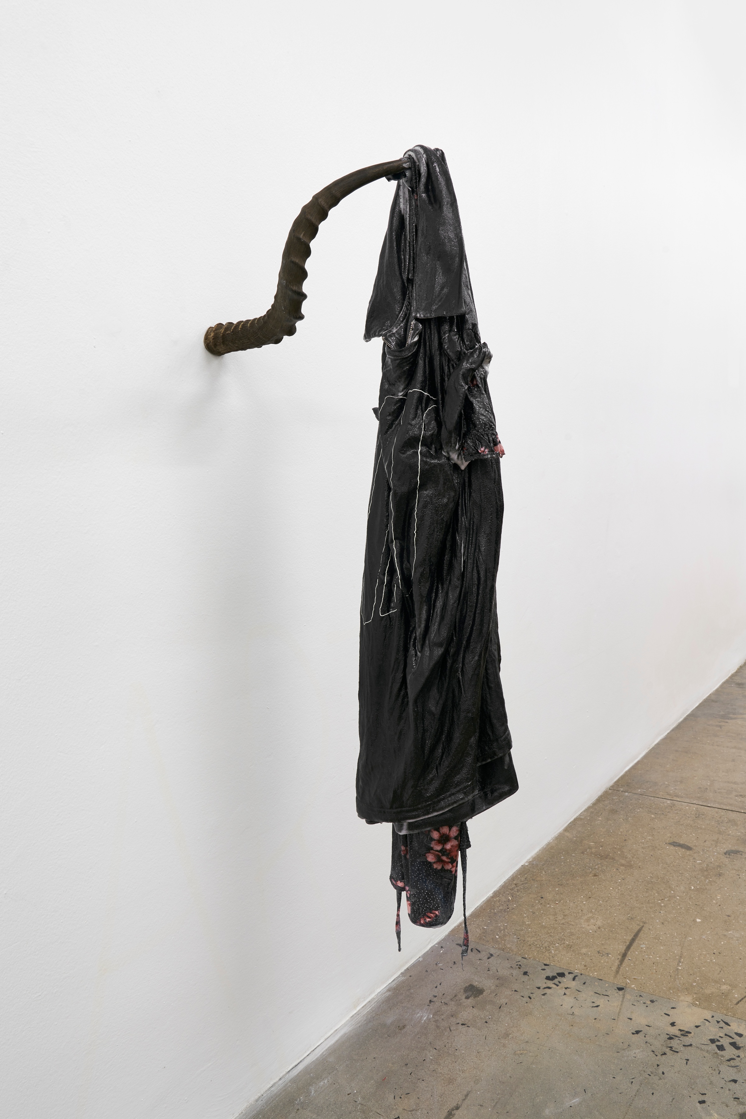 A photograph of Kevin Beasley's untitled sculpture, consisting of resinous garments suspended from a wall-mounted Antelope horn.
