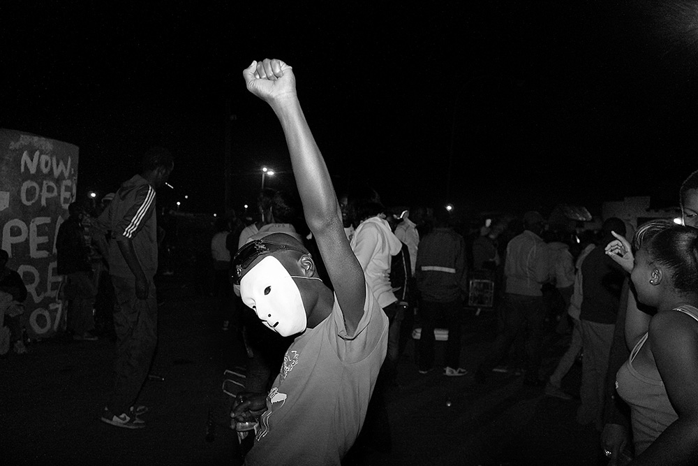 Photographic artwork from ‘Crossing Night: Regional Identities x Global Context’ exhibition at the Museum of Contemporary Art Detroit. Musa N. Nxumalo’s ‘Untitled (12),’ from their In/Glorius series, depicts a youth in a crowd with raised outstretched arm and wearing a mask.
