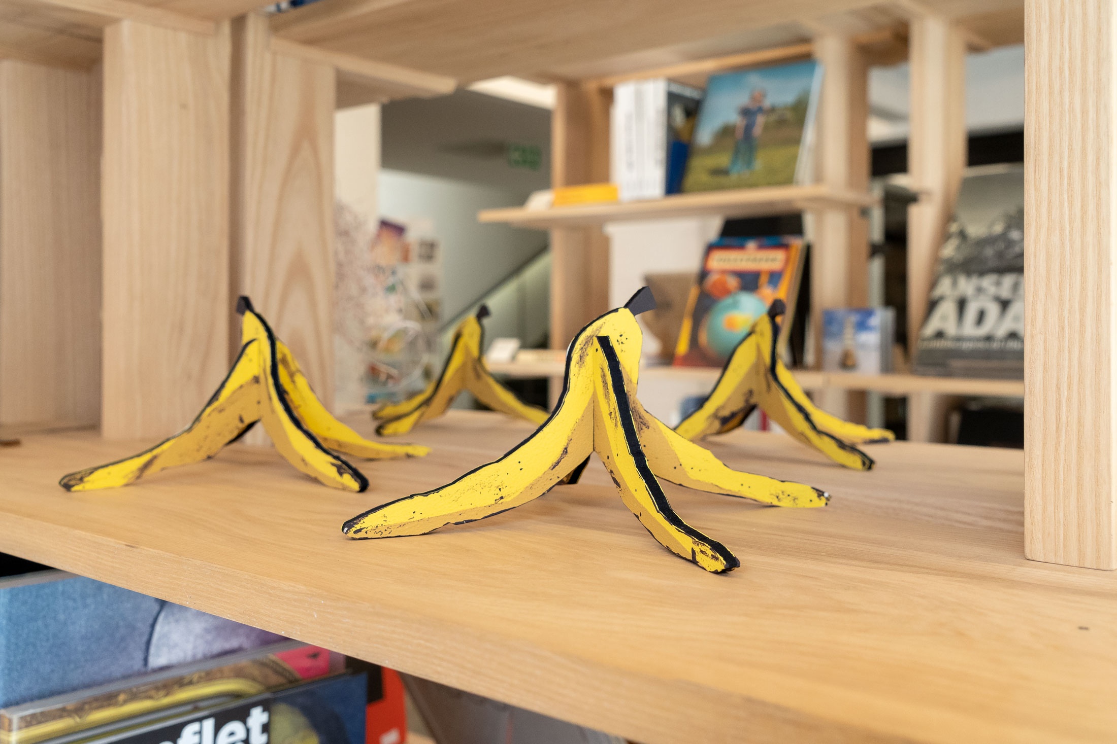 Installation photograph of four of Guy Simpson's painted MDF board sculptures 'Banana' on a shelf in A4 Arts Foundation's Proto museum store.
