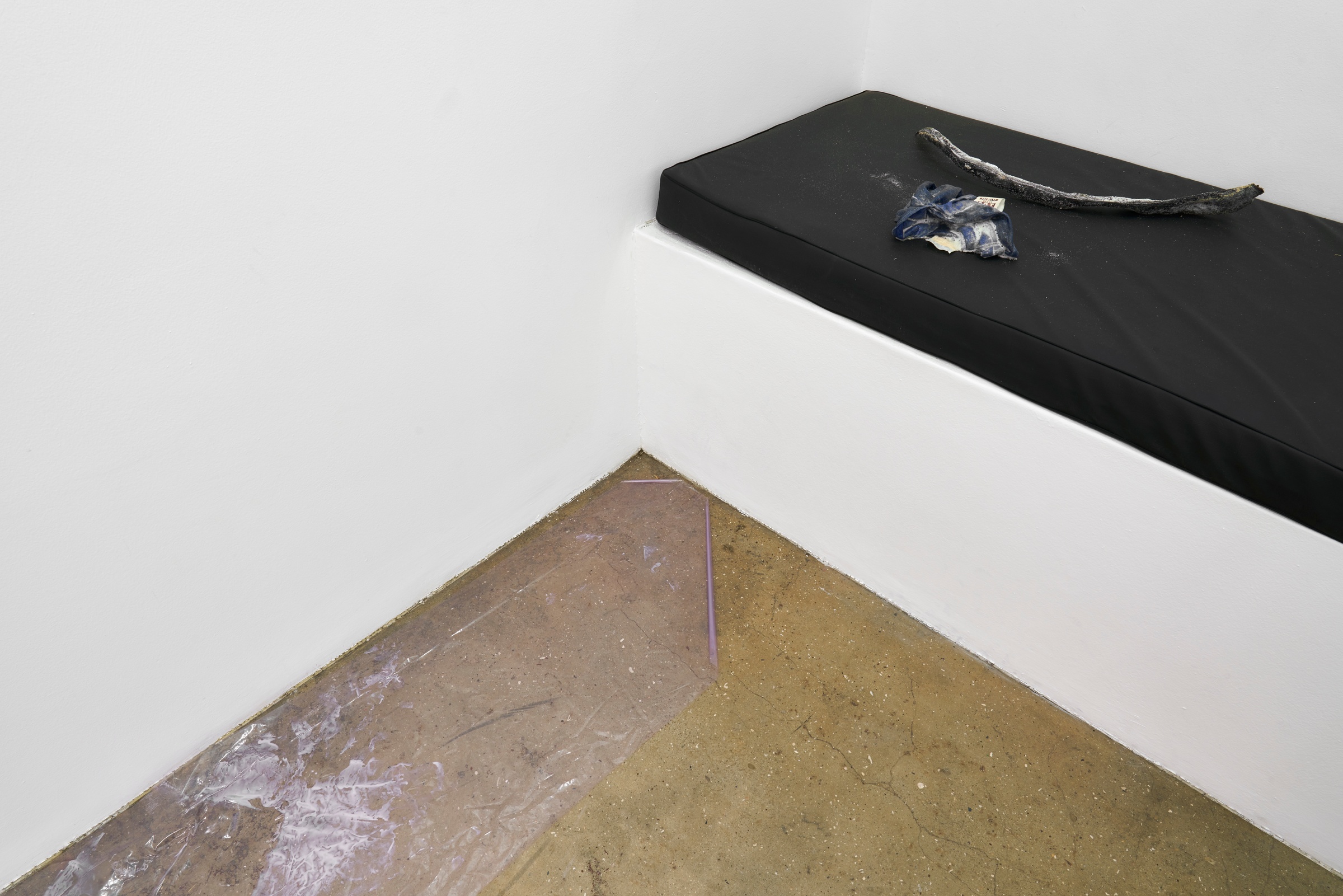 A photograph of Kevin Beasley's untitled resin, t-shirt, luggage, seaweed and heat-forming plastic sculpture sitting on a black cushion seat.
