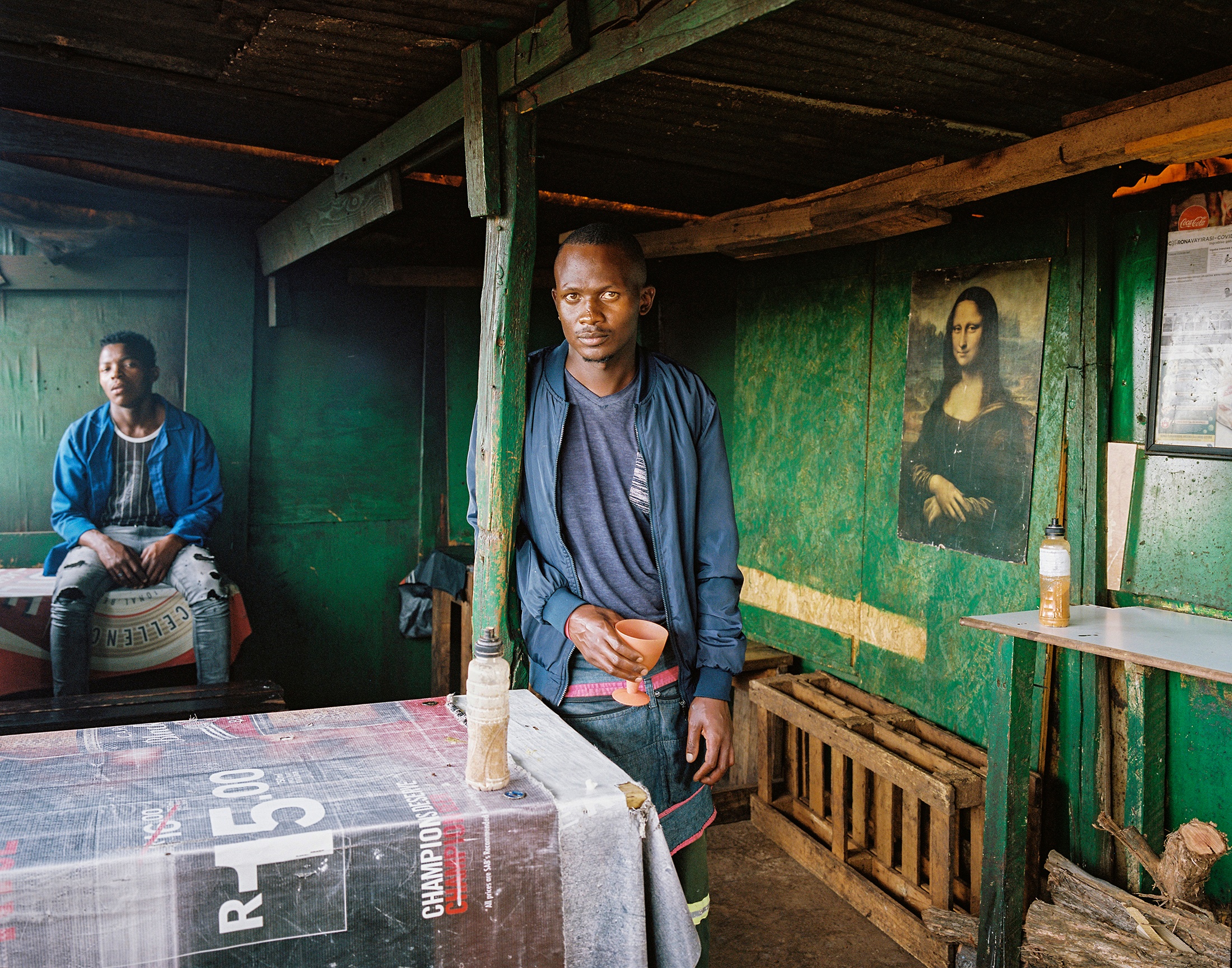 Lindokuhle Sobekwa's photograph 'Mona Lisa gaze' shows two individuals, one standing and one seated, in a building that features a print of Leonardo da Vinci's 'Mona Lisa' mounted on a wall.
