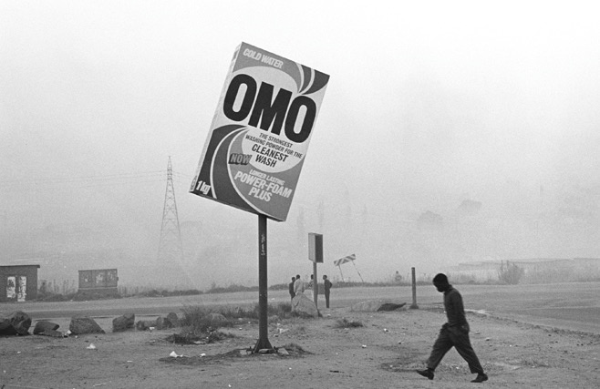 Santu Mofokeng's monochrome photographic print 'Winter in Tembisa' shows a slightly skew billboard for laundry detergent in a misty landscape.
