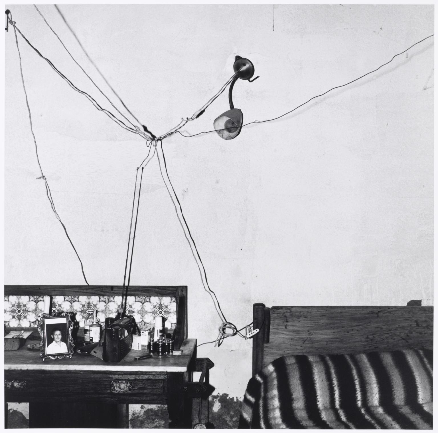 Roger Ballen’s monochrome photograph ‘Bedroom of Railway Worker, De Aar’ depicts a web of electrical cables pinned to a bedroom wall.
