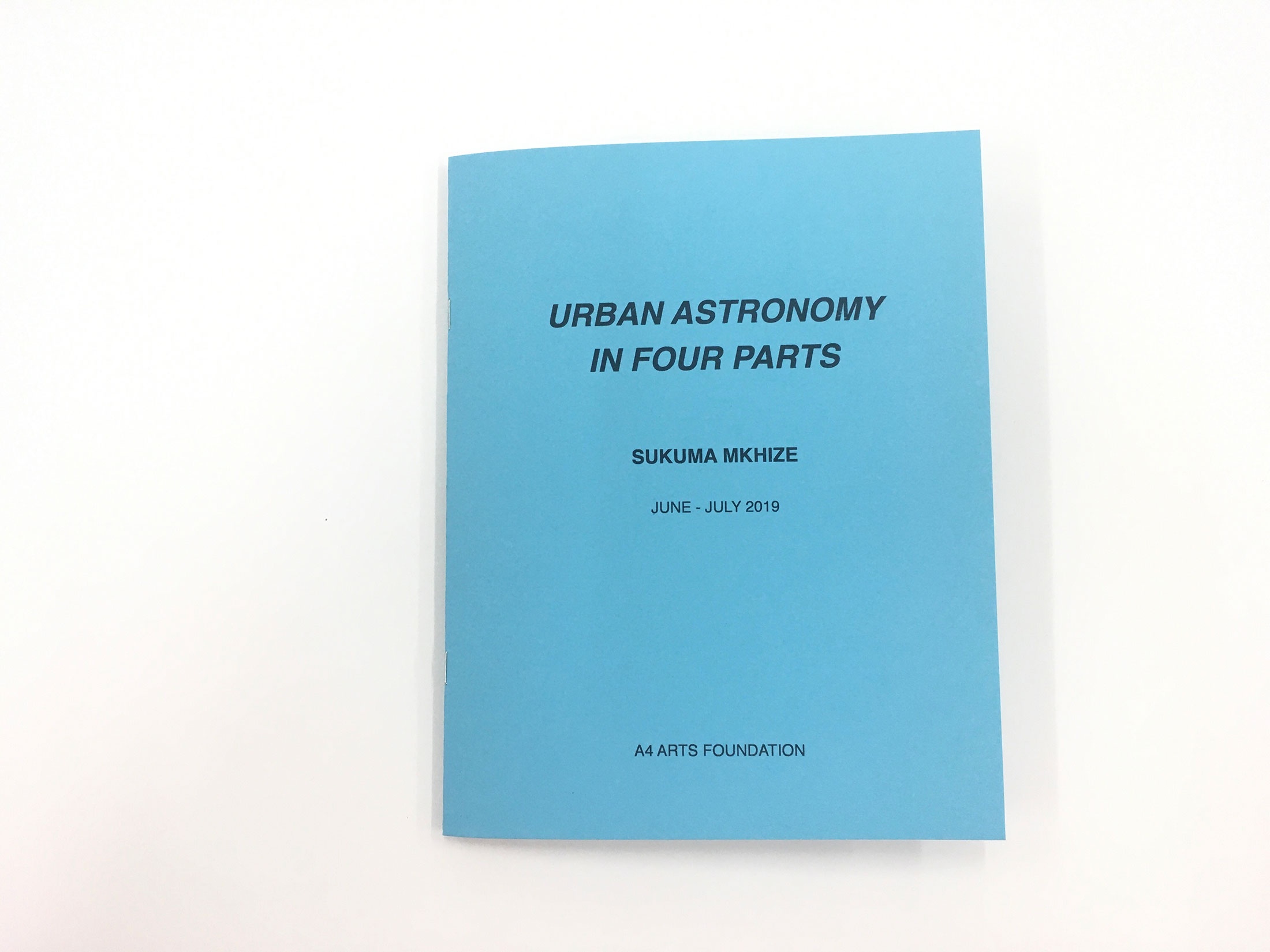 Photograph of ‘Urban Astronomy in Four Parts,’ a zine by Sukuma Mkhize from his residency at A4. The blue cover reads ‘Urban Astronomy in Four Parts, Sukuma Mkhize, June - July 2019, A4 ARTS FOUNDATION.’
