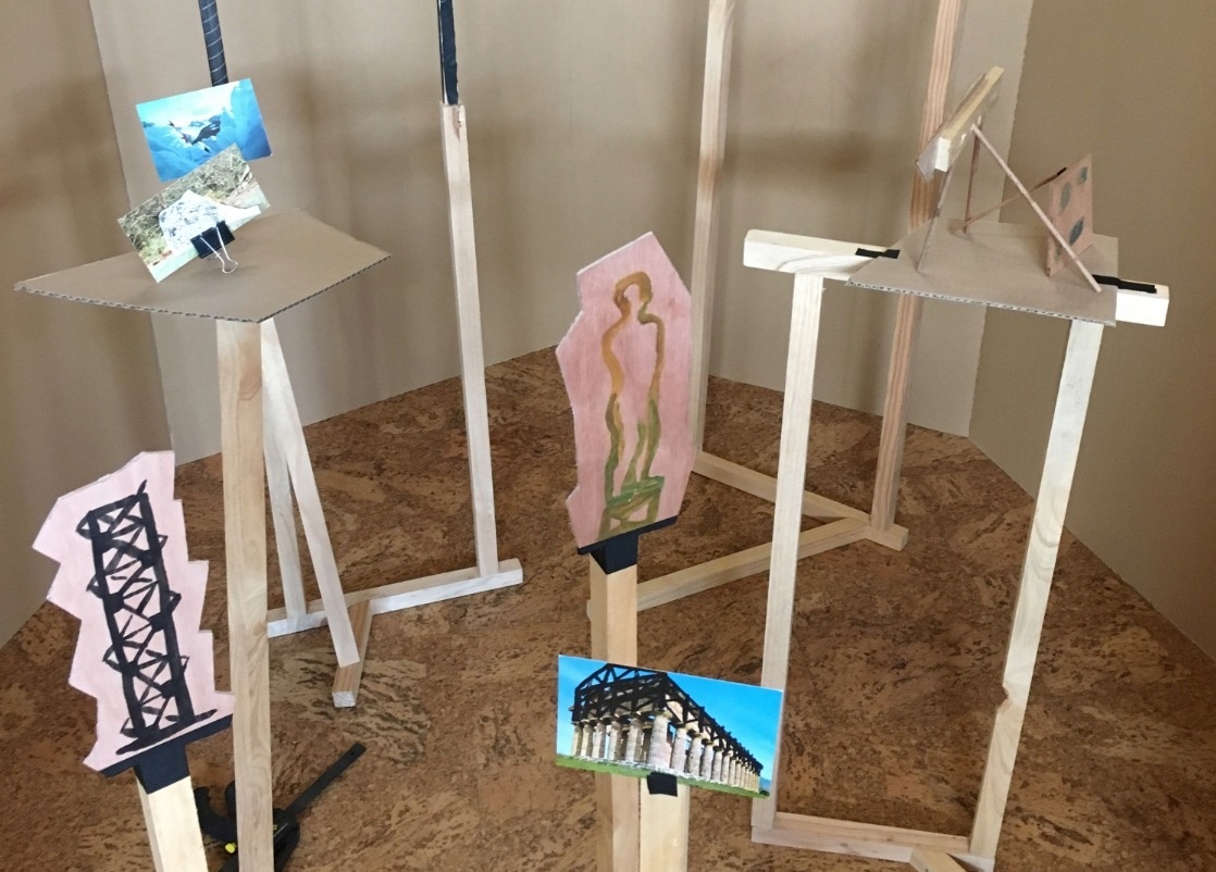 Process photograph from Jonah Sack’s residency on A4’s top floor. Small photographs and irregularly shaped paintings are mounted on spindly wooden stands in a cardboard enclosure.
