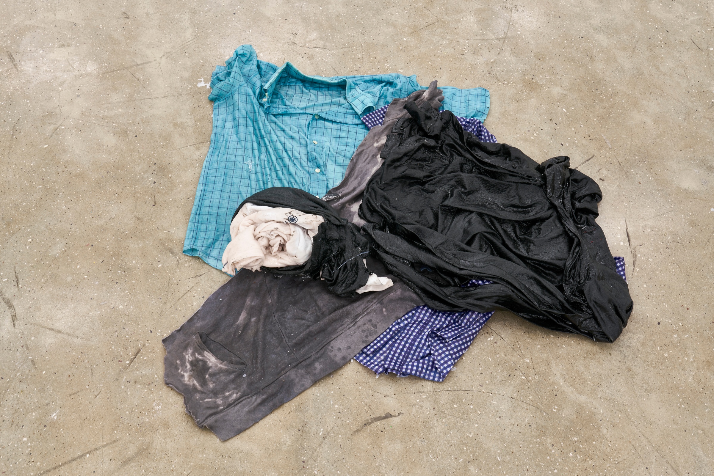 A photograph of Kevin Beasley's untitled resin and garment sculpture lying on a concrete floor.
