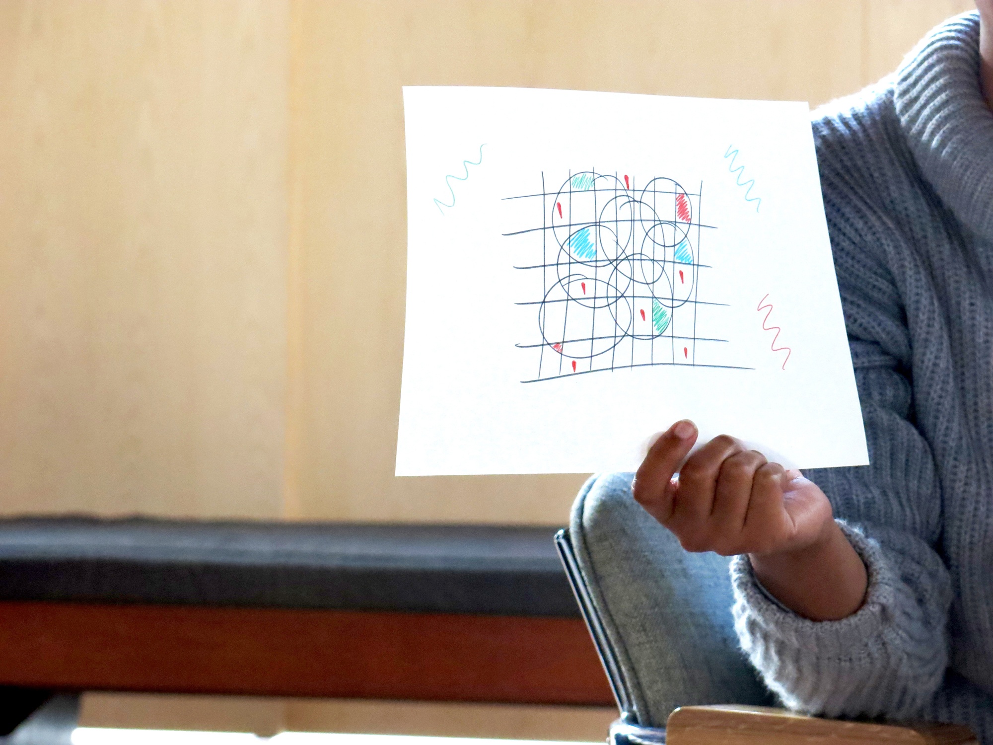 Event photograph from the 2018 rendition of the City Research Studio exchange with the African Centre for Cities. An individual is holding a paper with a felt pen marker drawing that consists of a grid with overlapping circles and drawing marks of various colours.
