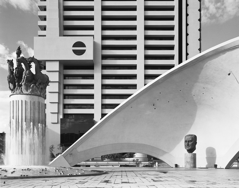 David Goldblatt's black-and-white photograph 'The monument at left celebrates the fifth anniversary of the Republic of South Africa. The one at right is to J G Strijdom, militant protagonist of White supremacy and of an Afrikaner republic, who died in 1958. At rear is the headquarters building of Volkskas (‘The People’s Bank’) founded in 1934 to mobilise Afrikaner capital and to break the monopoly of the ‘English’ banks. Pretoria, 25 April 1982' shows an architectural scene with buildings and statues.
