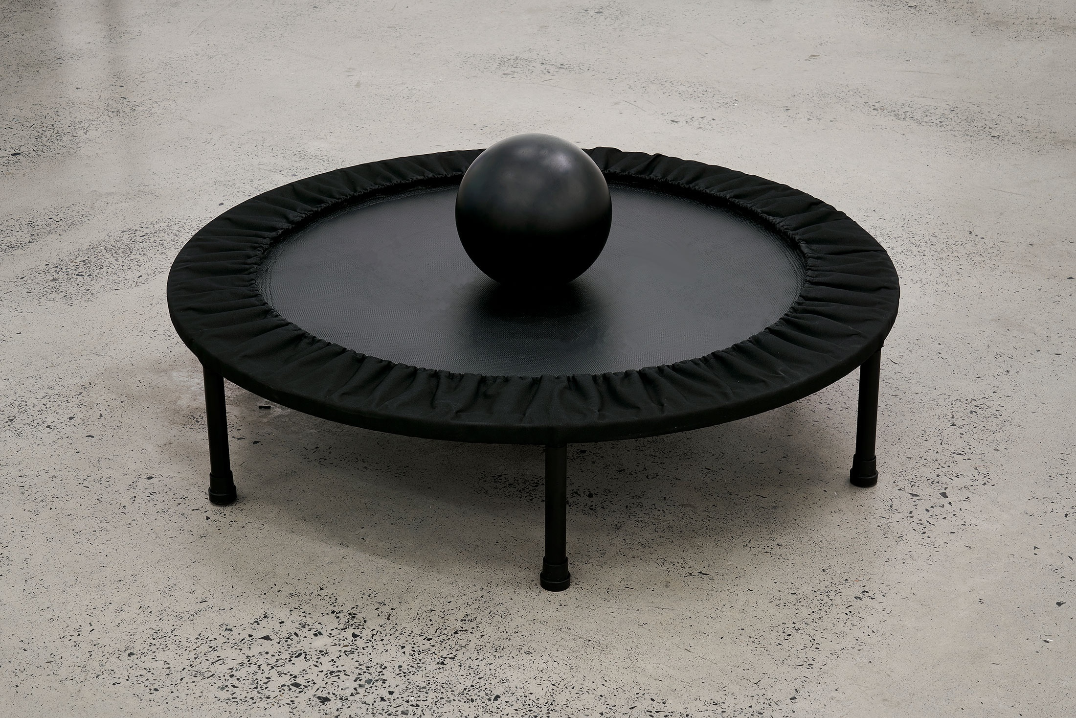 Installation photograph from the ‘Model’ exhibition in A4’s Reading Room. Bogosi Sekhukhuni's trampoline and bowling ball 'Dark Gravity' sits on a concrete floor.
