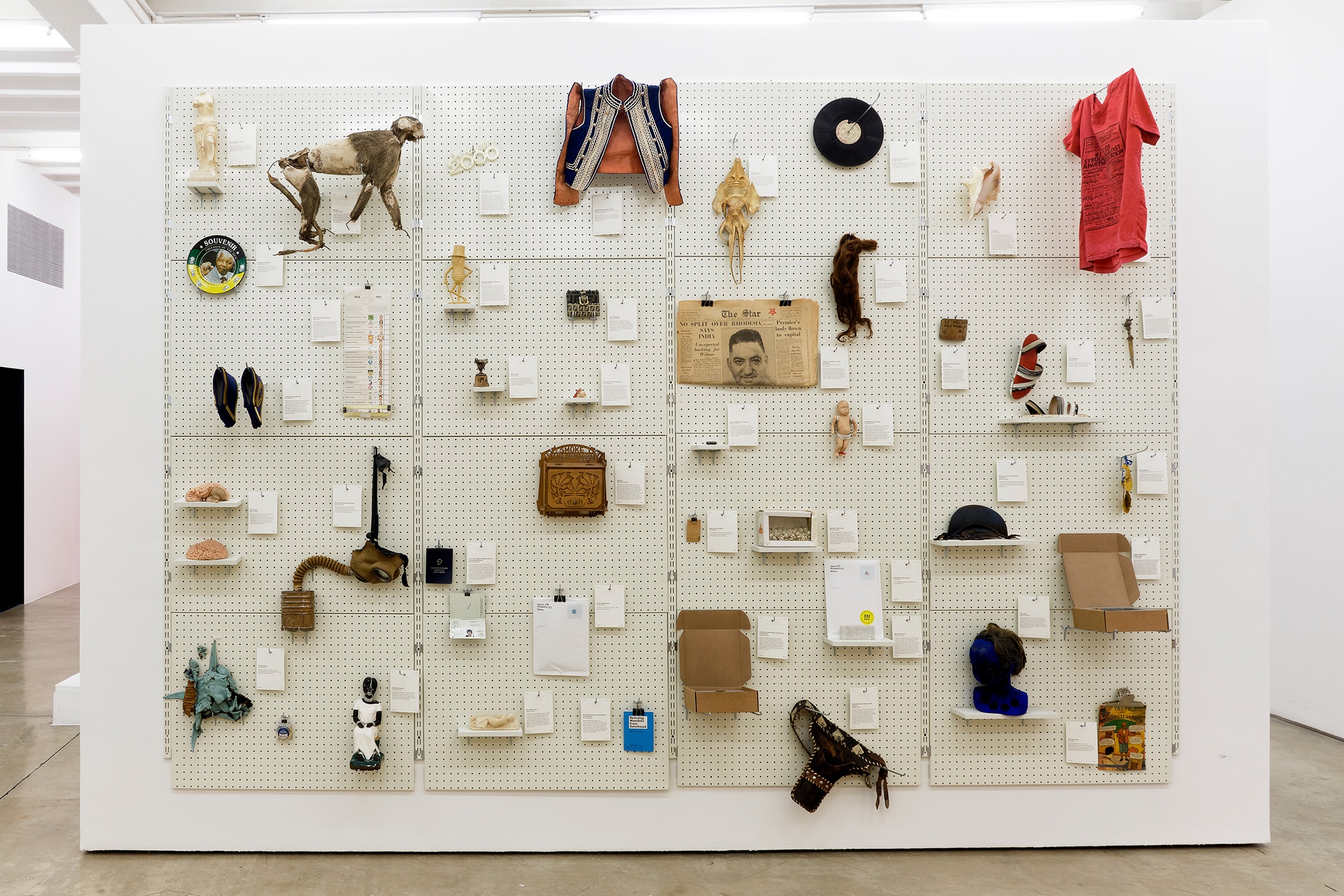Installation photograph from the 'A Little After This' exhibition in A4 Arts Foundation's gallery that shows collected objects from Penny Siopis' 'Will' work mounted on a white moveable gallery wall through the use of perforated metal panels.
