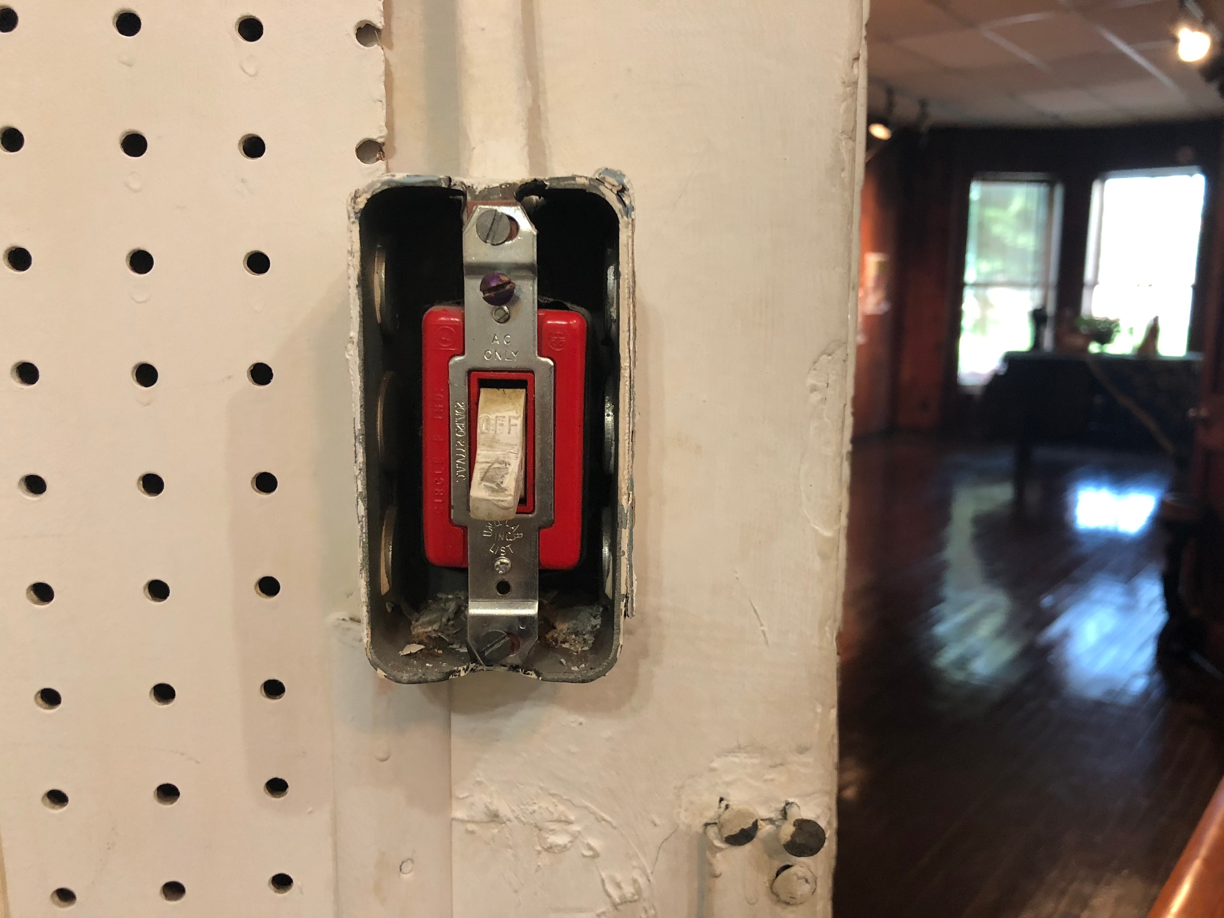 Ephemera from the offsite event ‘On Curating: Institutions and their Social Fabrics’ at the Art Institute of Chicago. An electric light switch without a cover sits on a perforated white wall.
