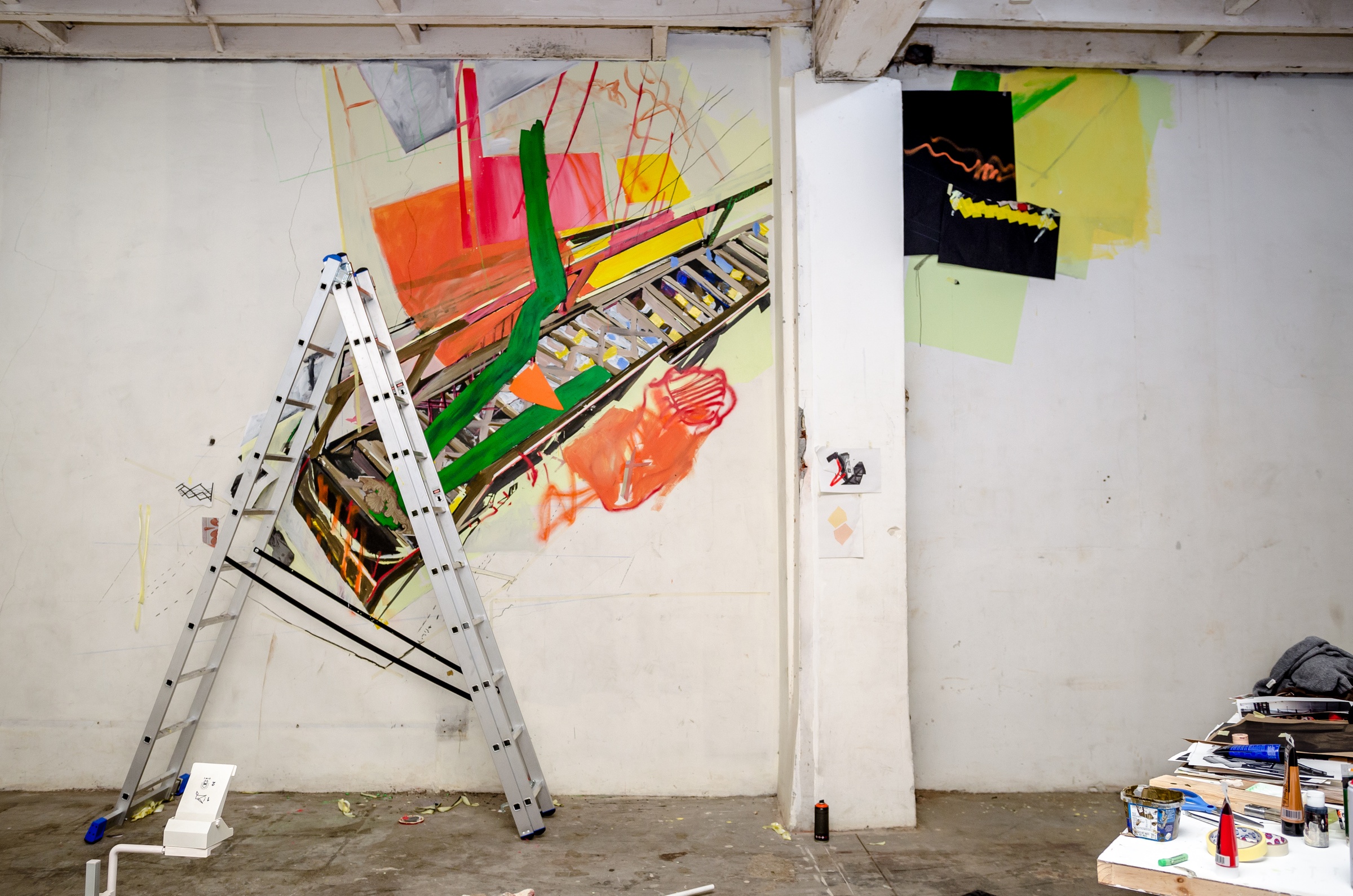 Process photograph from Dorothee Kreutzfeldt’s residency on A4’s 1st floor. At the back, the wall features a painted mural along the top. At the front, a folding ladder stands in front of the wall.
