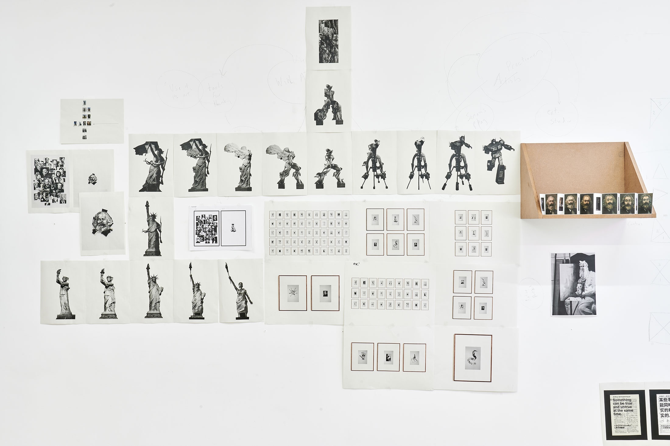 Process photograph from Patrick Waterhouse's 2022 residency in A4 Arts Foundation's studio shows photographic prints on paper arranged along the studio wall, and on a wooden wall-mounted shelf.
