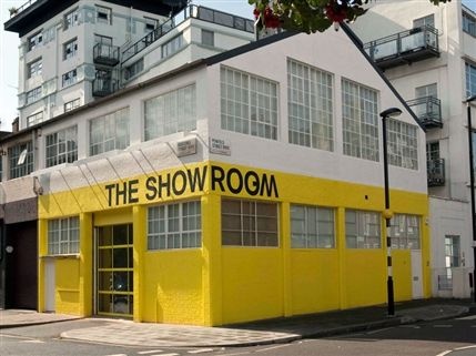 Photograph of the The Showroom gallery in London from Emily Pethick’s visit to Atlantic House studios. The building has a v-shaped roof, with the top floor painted white and the ground floor painted yellow.

