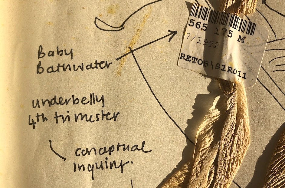 Process photograph from the 2019 rendition of the CCA Internship Programme on A4’s top floor, depicting a detail of a page. On the left, snippets of felt pen writing and diagrammatic drawings. The text fragments read “Baby Bathwater”, “underbelly 4th trimester” and “conceptual inquiry.” On the right, a barcode sticker holds a strand of unknown material to the page.
