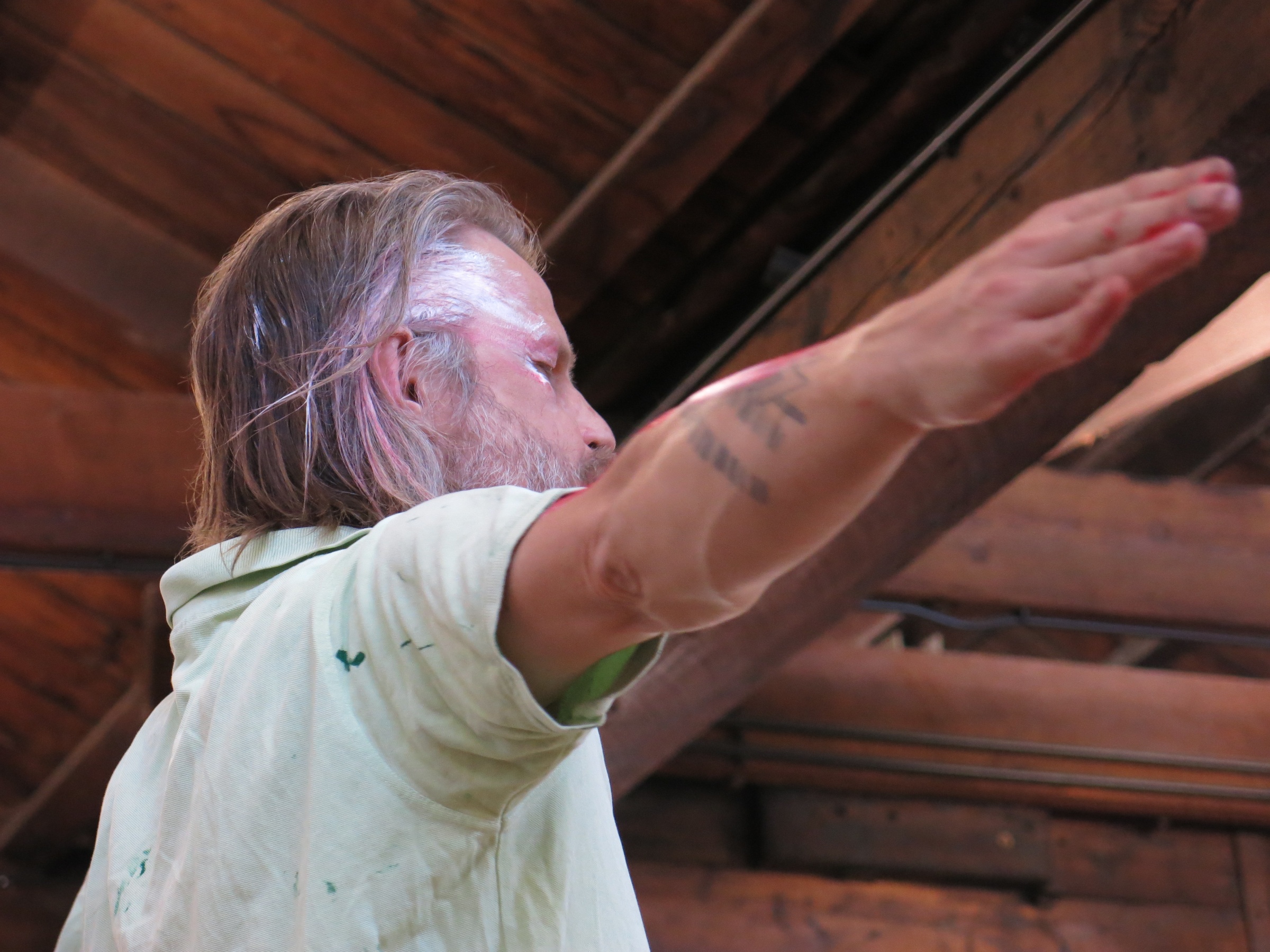 Event photograph from Mårten Spångberg’s solo dance ‘Digital Technology’ on A4’s top floor that shows Spångberg with his arms outstretched and paint on the side of his face.
