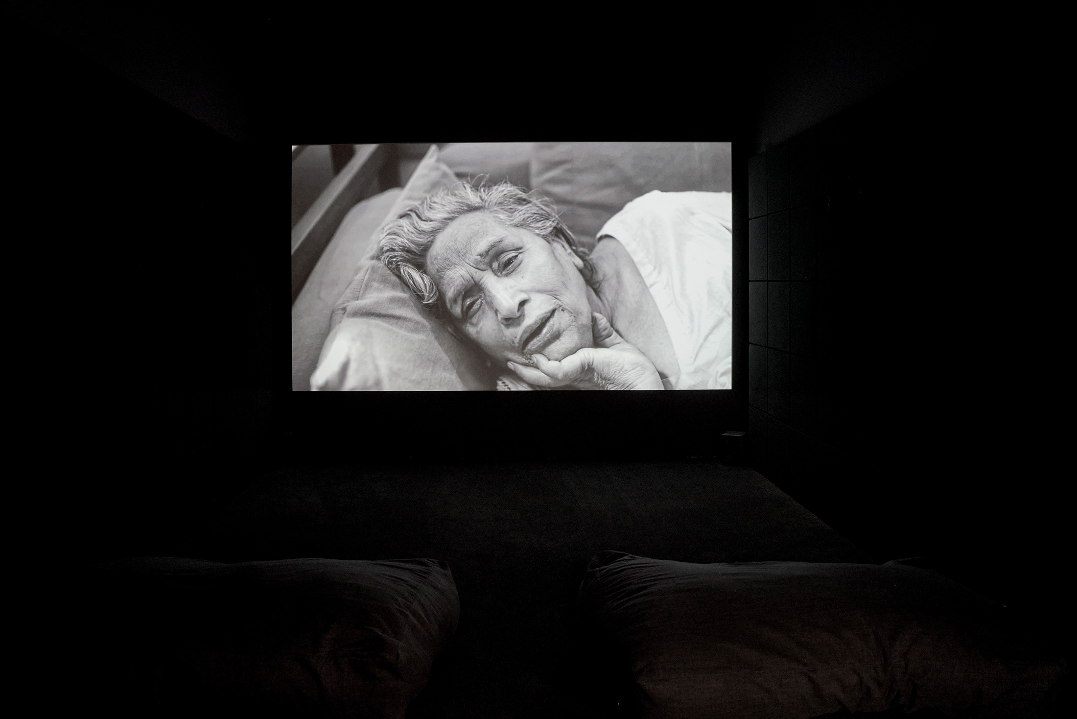 Installation photograph that shows Dayanita Singh’s video work ‘Mona and Myself’ projected onto a wall in a darkened room.
