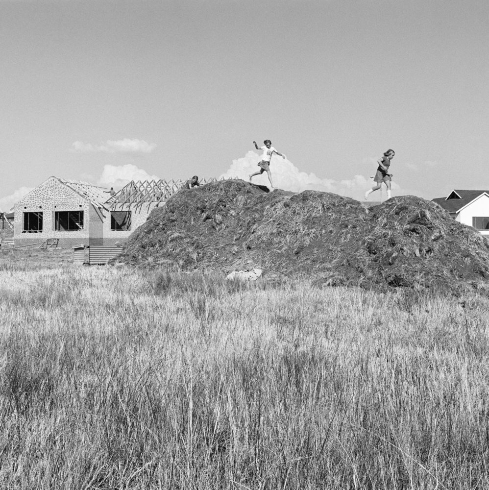 David Goldblatt's monochrome photograph 'Spec housing and children on the veld at Parkrand' shows children playing on a large mound of dirt.
