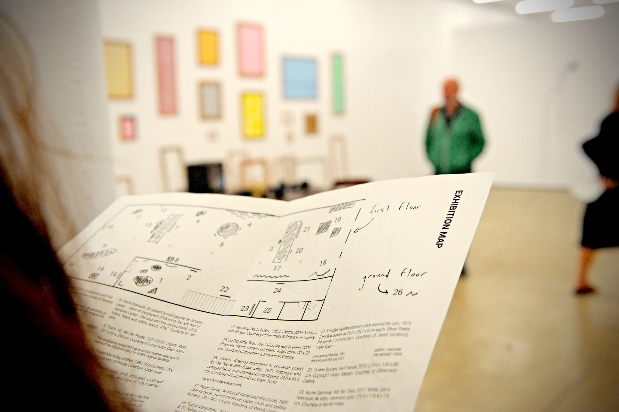 Event photograph from the More For Less exhibition in A4’s Gallery that shows an attendee holding an exhibition handout.
