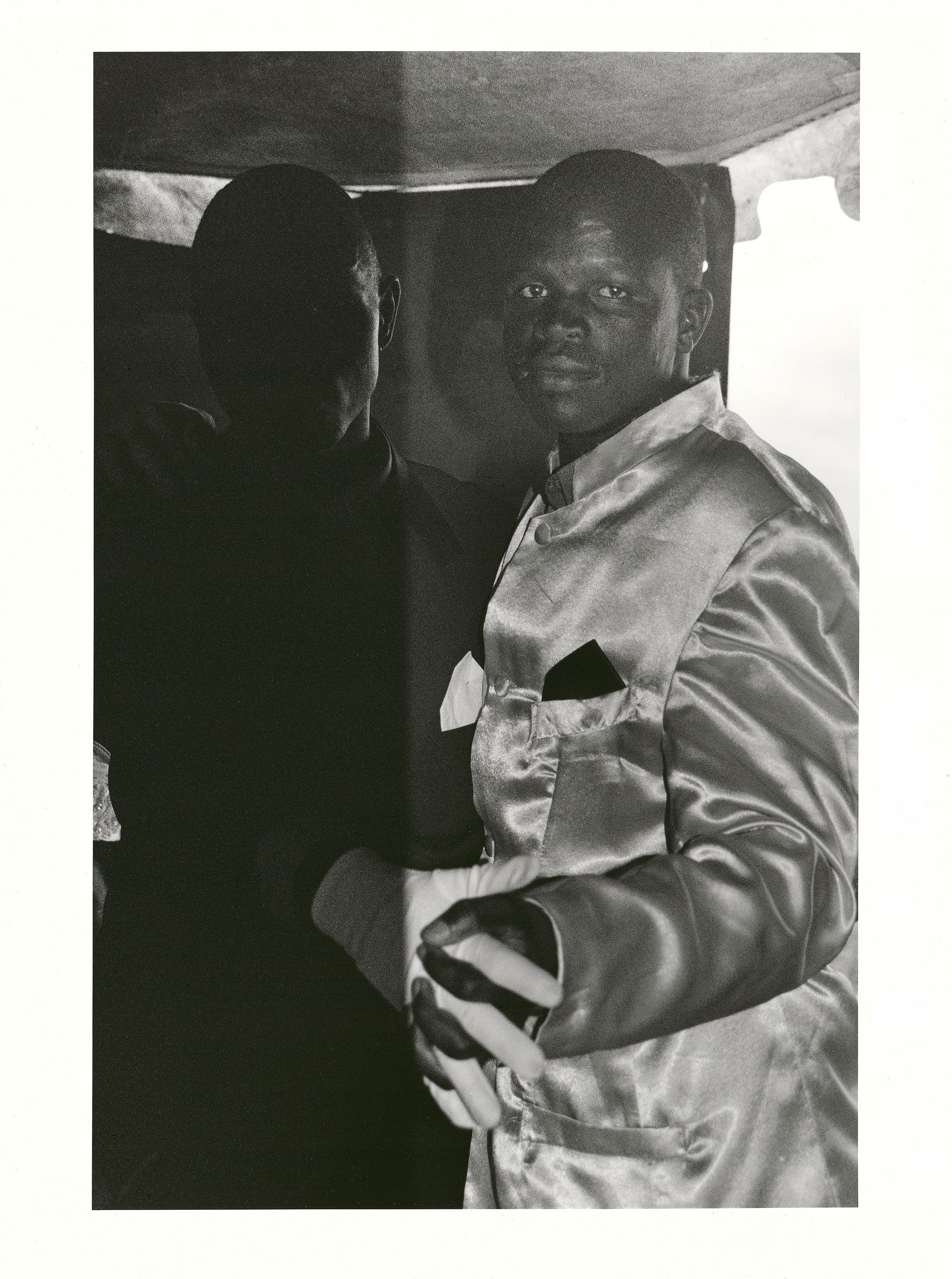 Sabelo Mlangeni’s ‘Impelesi enkulu Zakhele Maseko no Mkwenyana’, a black and white photograph depicting two people dancing at a wedding with the person on left in shadow. 
