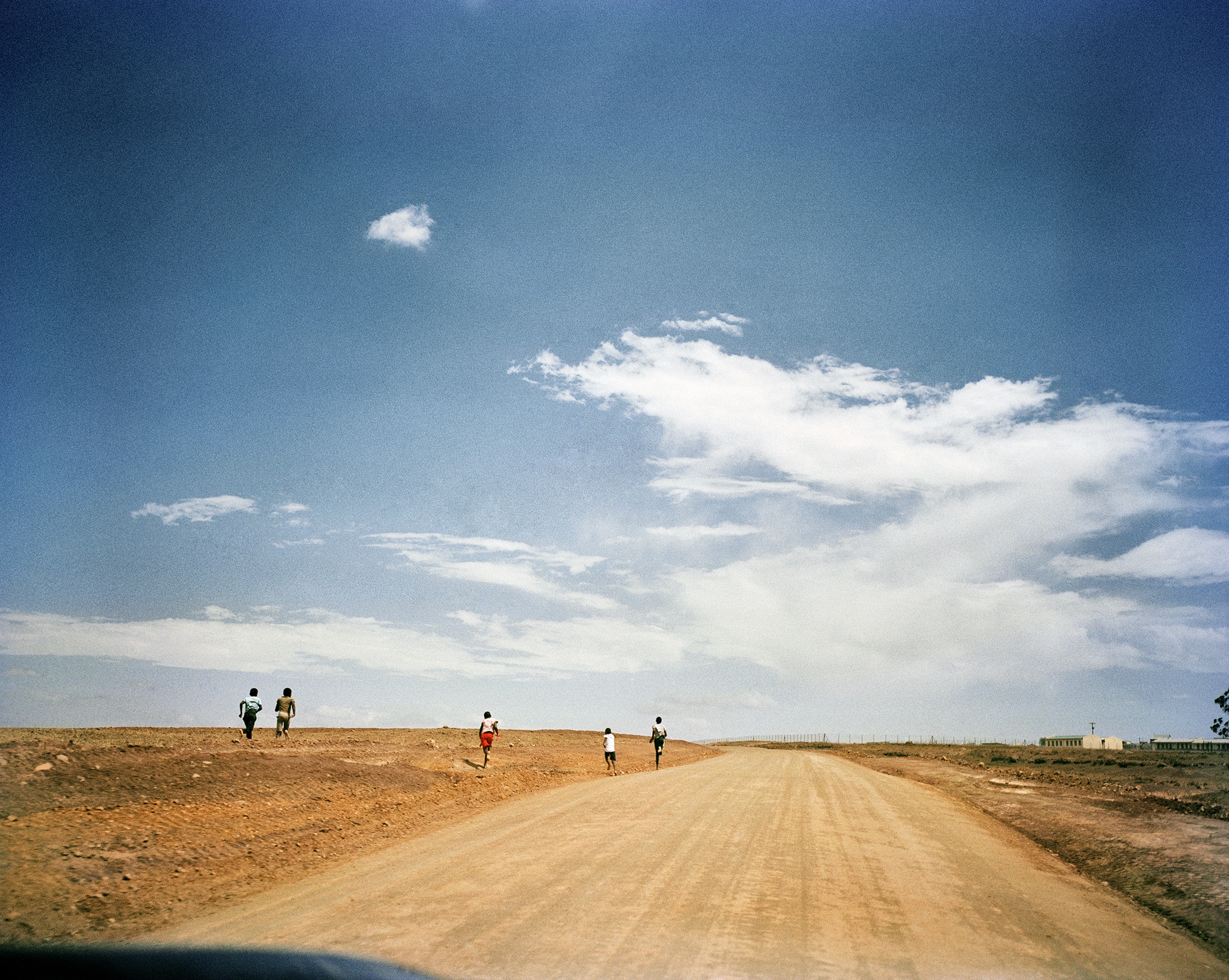 Lindokuhle Sobekwa's photograph 'Tsojana bus stop' shows children running next to a tarred road.
