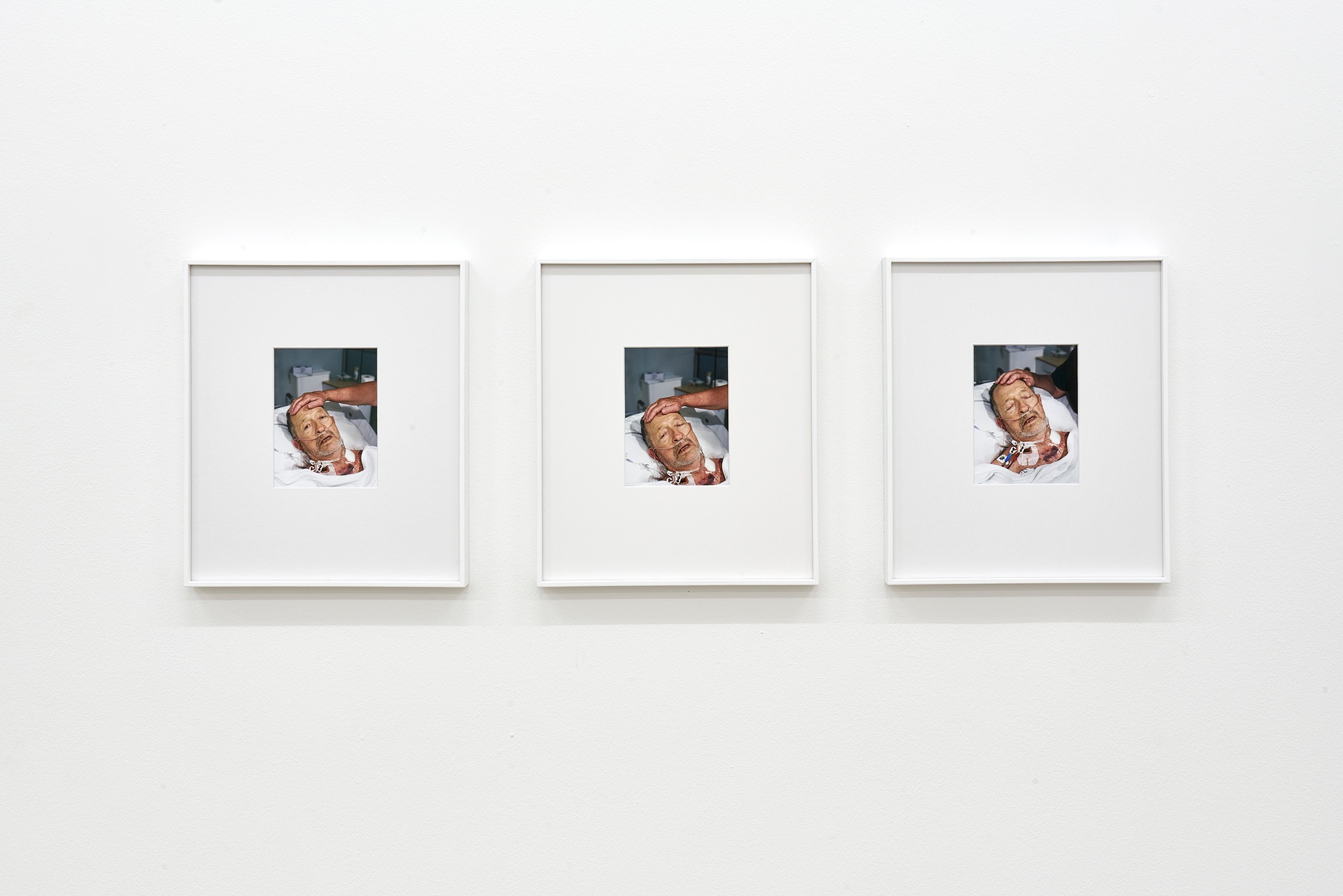 Installation photograph that shows Pieter Hugo’s framed photographic triptych ‘944-03-03, MALE, MARRIED, 2021-12-21, CAPE TOWN, NATURAL CAUSES’ mounted on a white wall.
