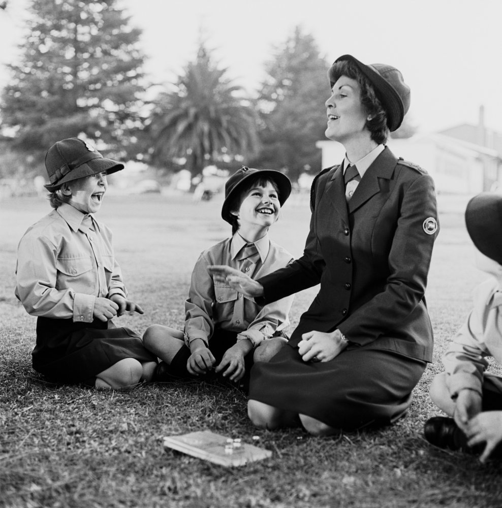David Goldblatt's monochrome photograph 'At a meeting of the Voortrekkers in the suburb of Whitfield, Boksburg. June 1980' shows a woman and children kneeling on a grassy lawn.
