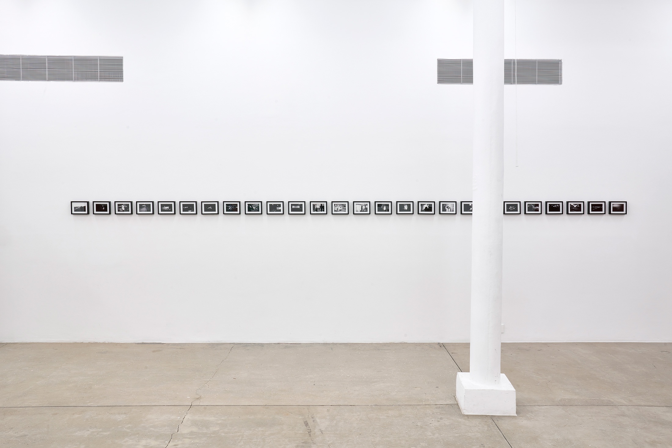 Installation photograph that shows Bas Jan Ader's photographic series 'Study for In Search of the Miraculous (One Night in Los Angeles)' with 26 framed photographs mounted on a white wall in a straight line.
