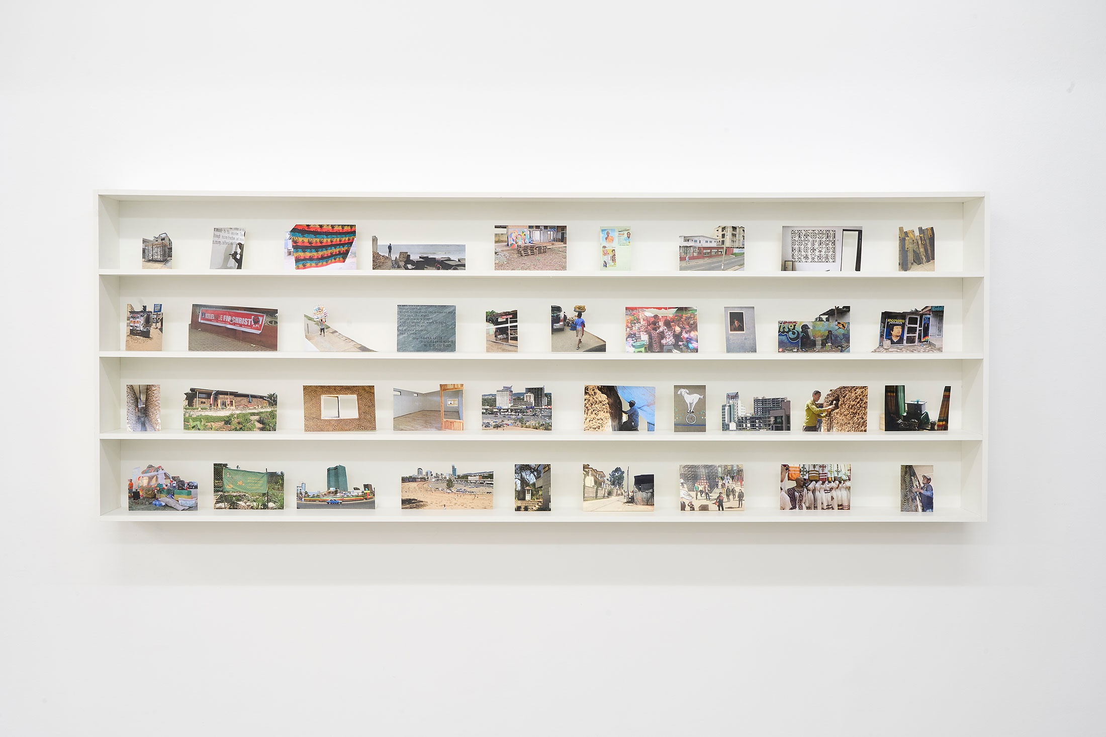 Installation photograph from the book launch of Kim Gurney’s ‘Panya Routes’ in A4’s Reading Room. A white bookshelf mounted on the wall is lined with photographs from the book.
