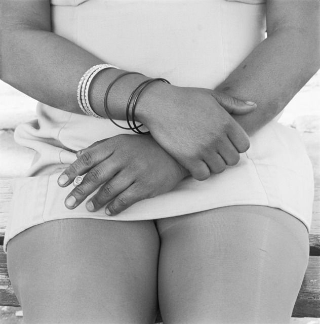 David Goldblatt's monochrome photograph 'Woman smoking, Fordsburg, Johannesburg. 1975' shows a seated woman, her hands folded in her lap, holding a cigarette.
