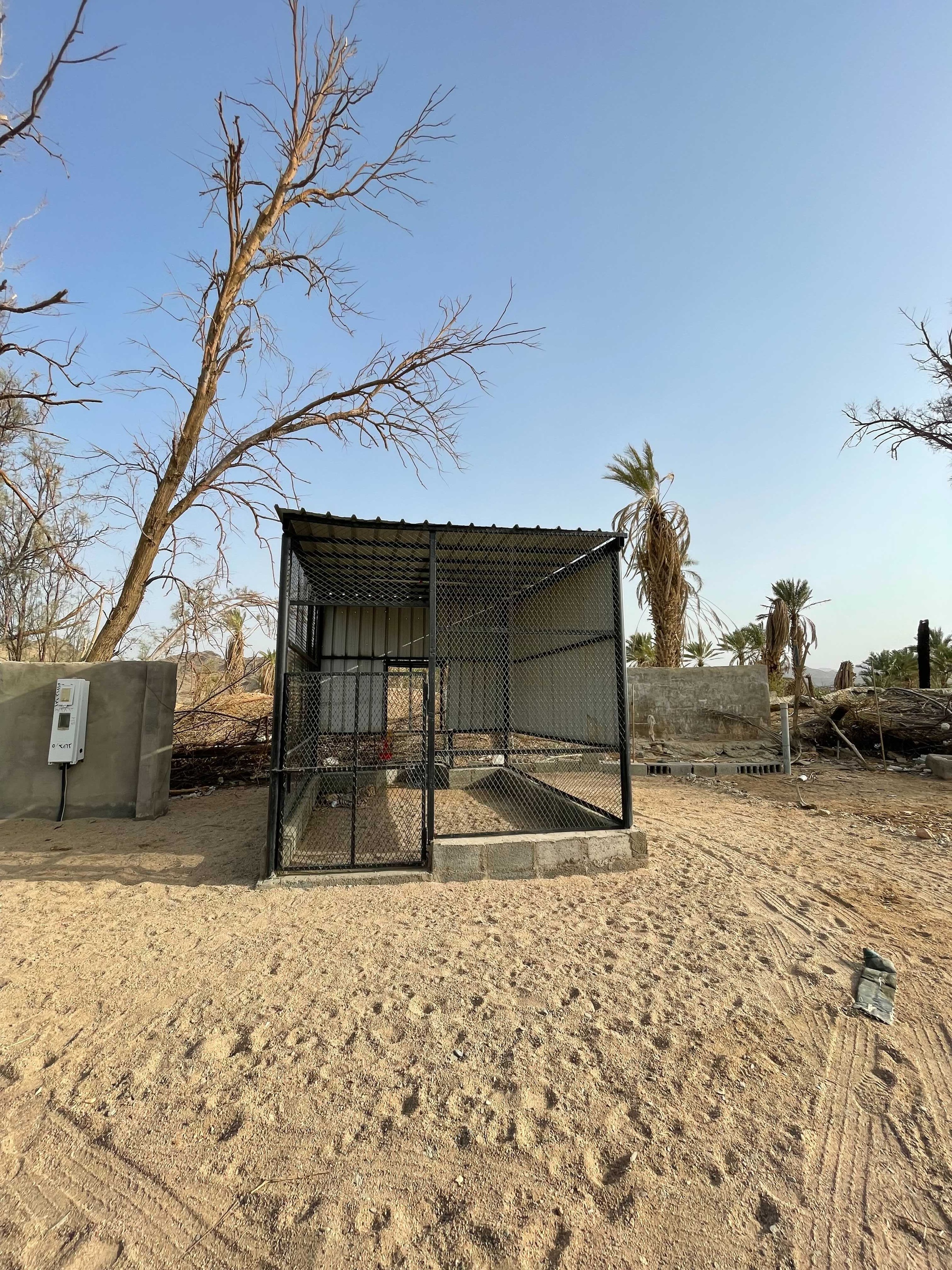 Process photograph from Waiting Upon, Sumayya Vally’s Course of Enquiry at A4, depicting a roadside mosque in Saudi Arabia. In the middle, a cubic structure made from metal beams, mesh and corrugated metal plates sits on a base outlined in brick.
