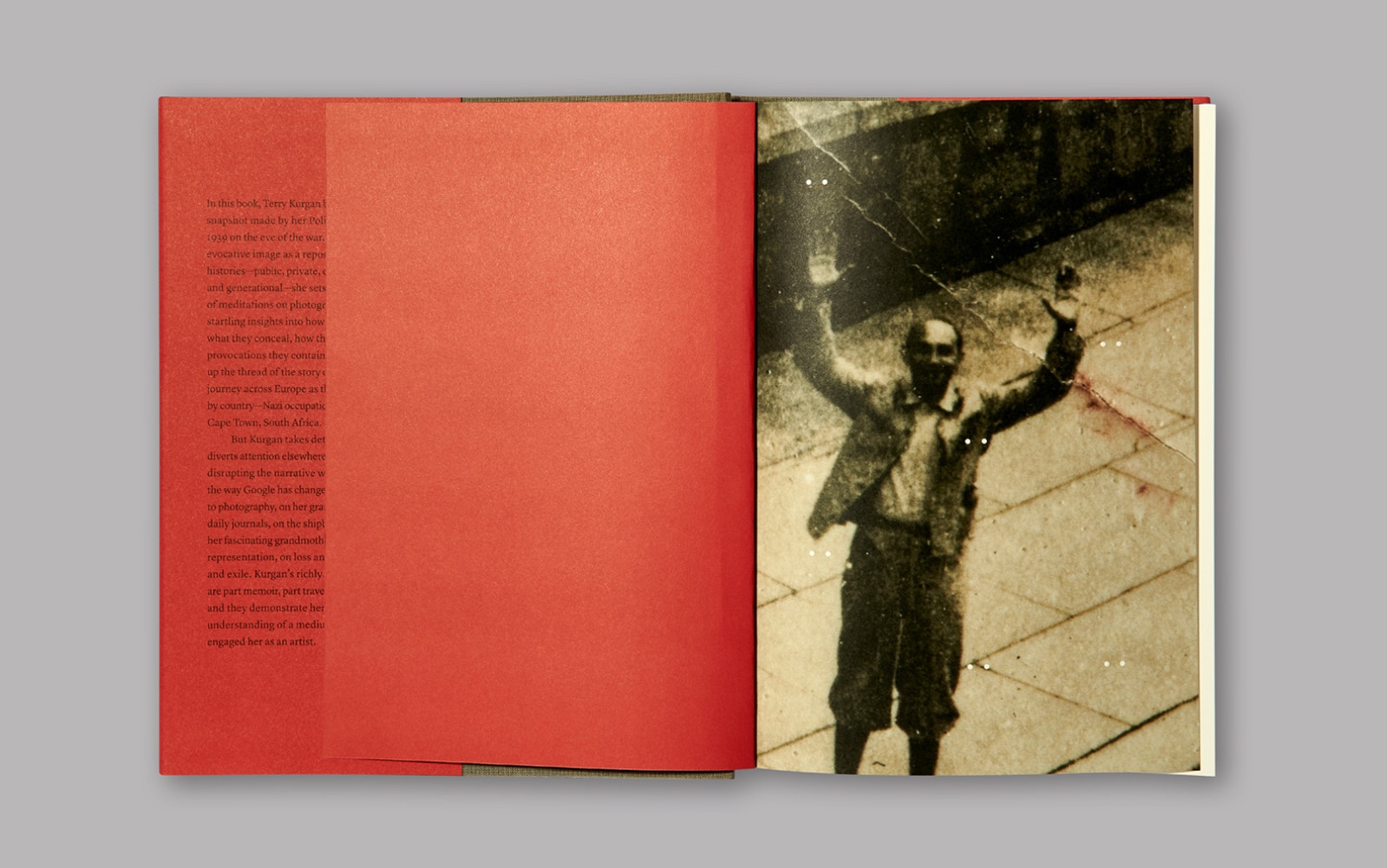 A topdown photograph of Terry Kurgan’s book ‘Everyone is Present: Essays on Photography, Memory and Family’ from the book launch on A4’s top floor. On the left, an empty red page. On the right, a full page photographic detail of a man with raised hands standing on a stone surface.
