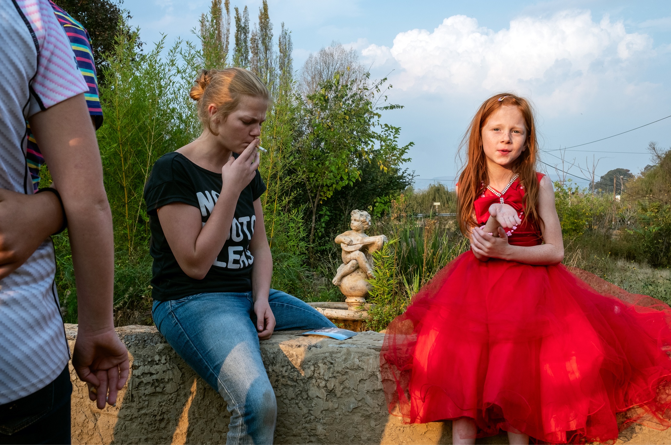 Lindokuhle Sobekwa's photograph 'Jeannie with her sisters' shows two children seated on a low stone wall, with a fountain in the back.
