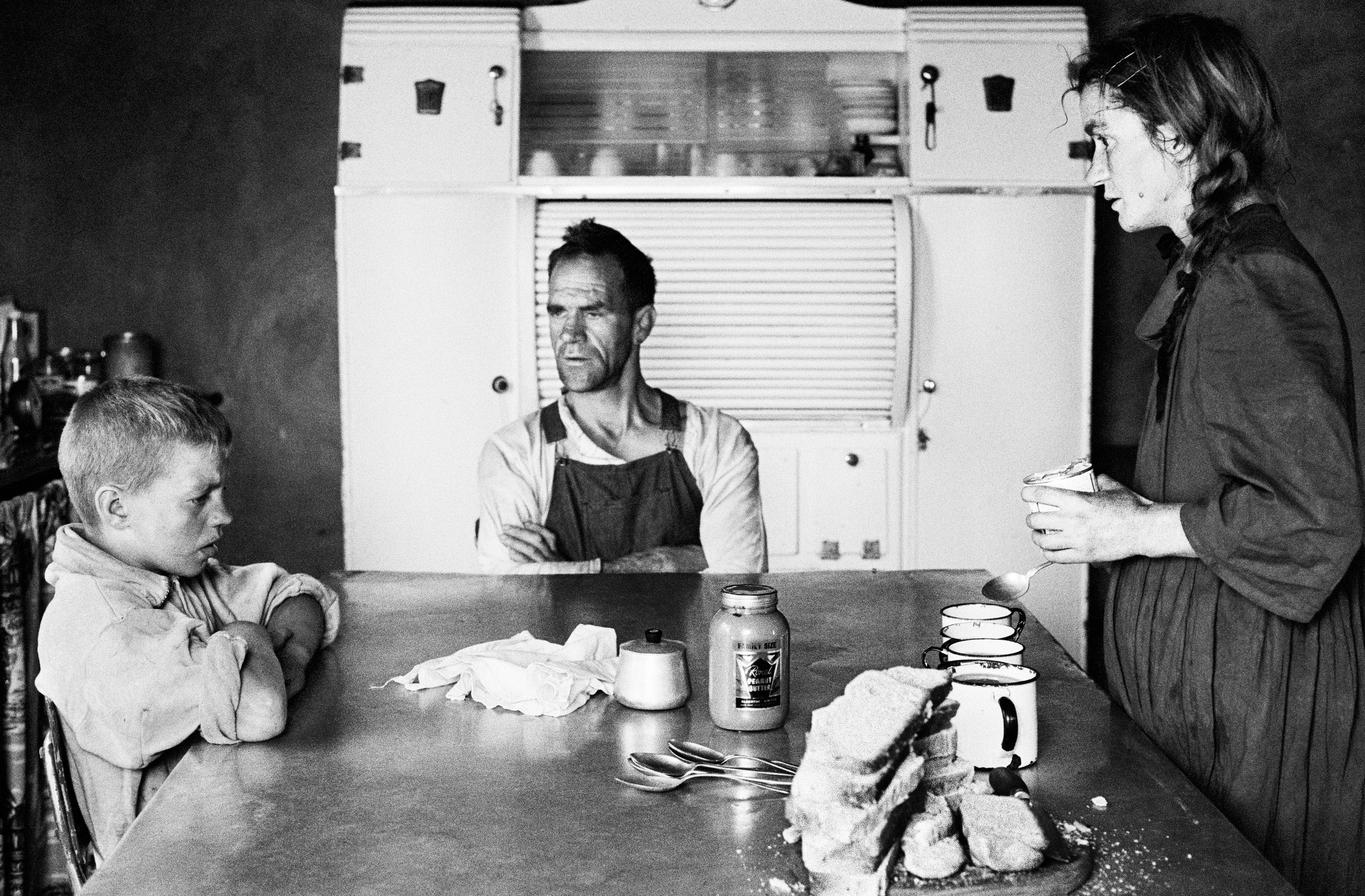 David Goldblatt's black-and-white photograph 'A plot-holder, his wife and their eldest son at lunch, Wheatlands, Randfontein' shows a family gathered around a table.
