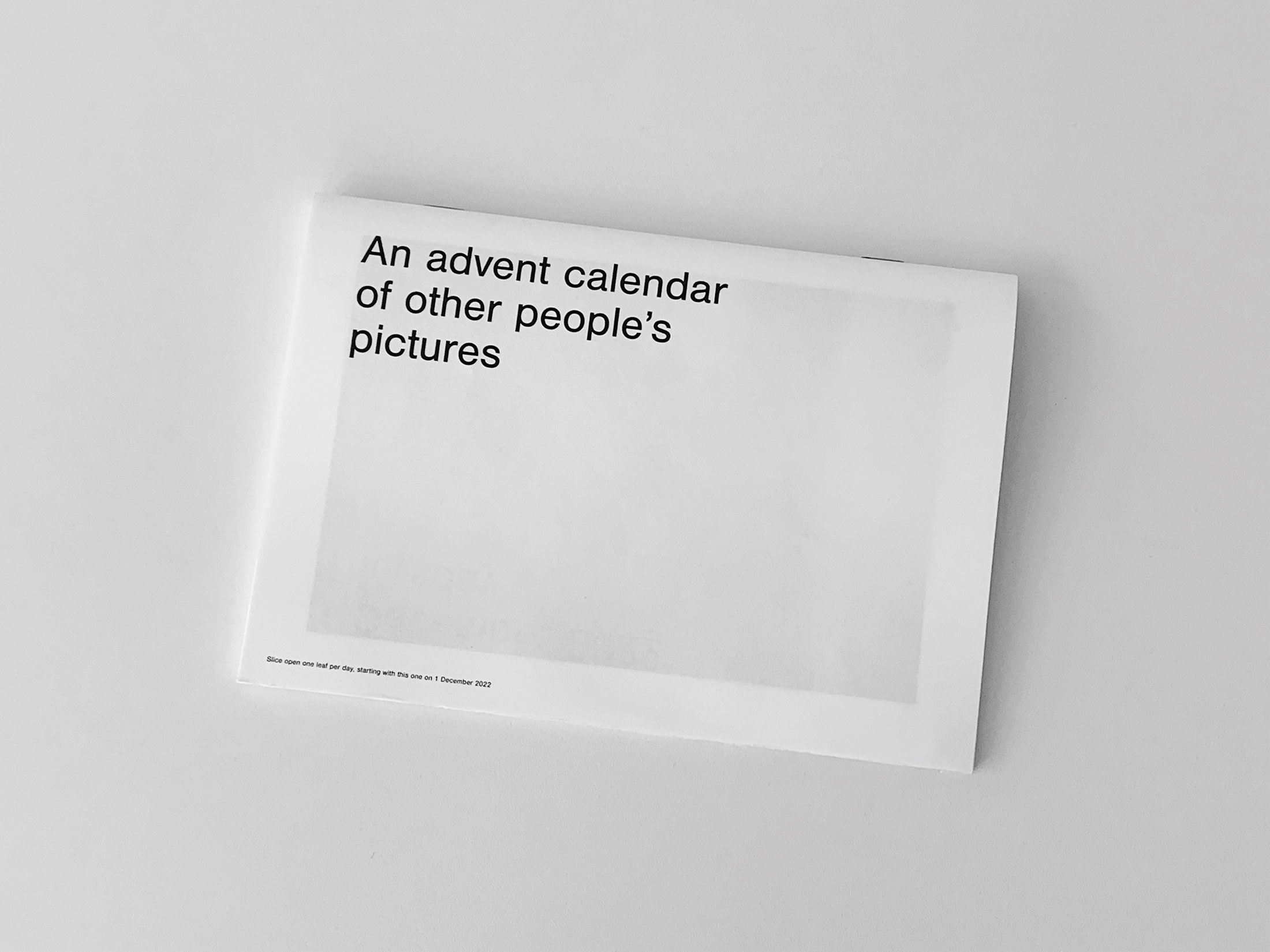 A photograph of Gabrielle Guy’s publication ‘An Advent Calendar of Other People’s Pictures.’ A rectangular printed calendar with a white front page and black text sits on a white background.
