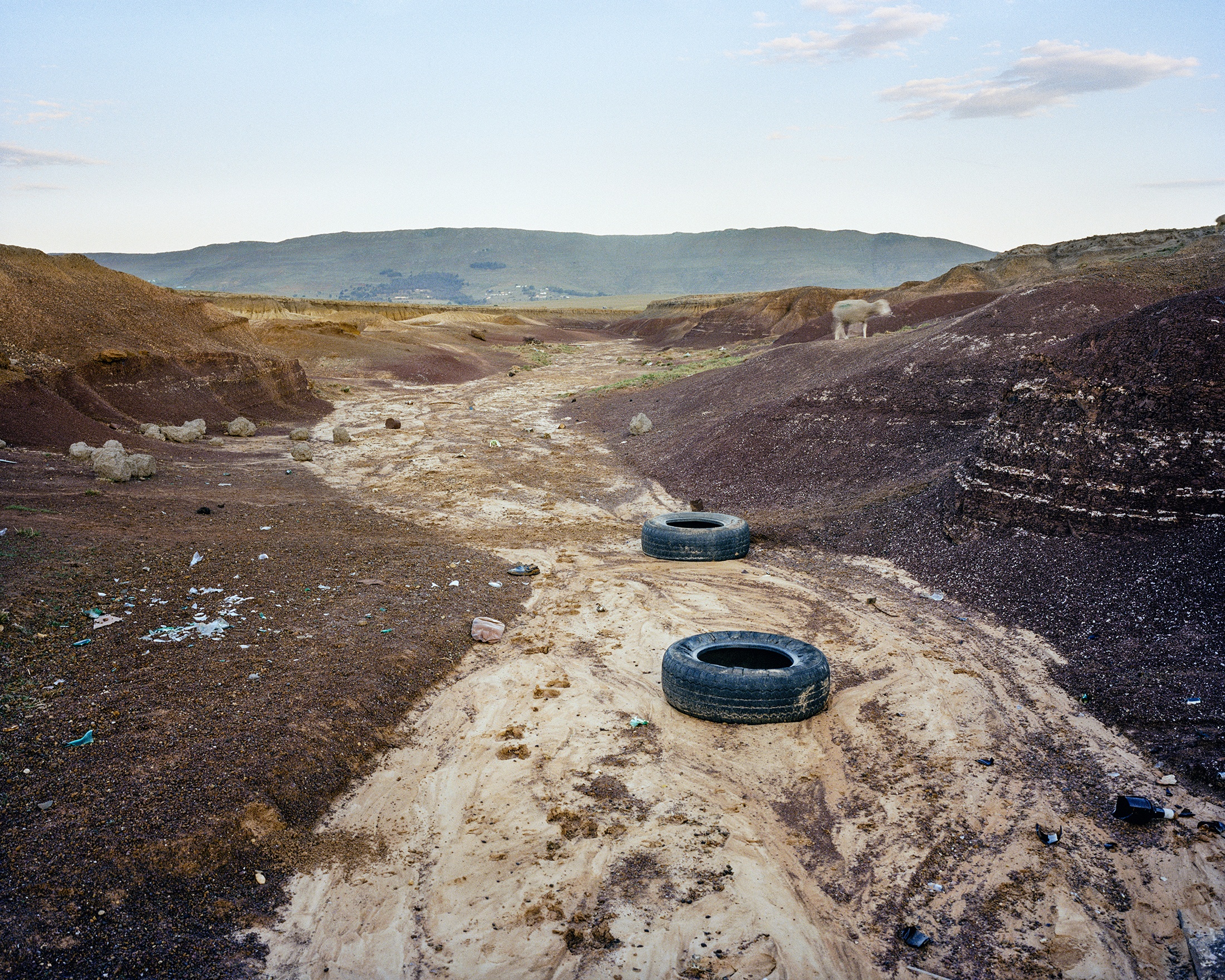 Lindokuhle Sobekwa's photograph 'Ezindongeni zase Khwezane' shows a dry riverbed with two tires lying on the sediment.
