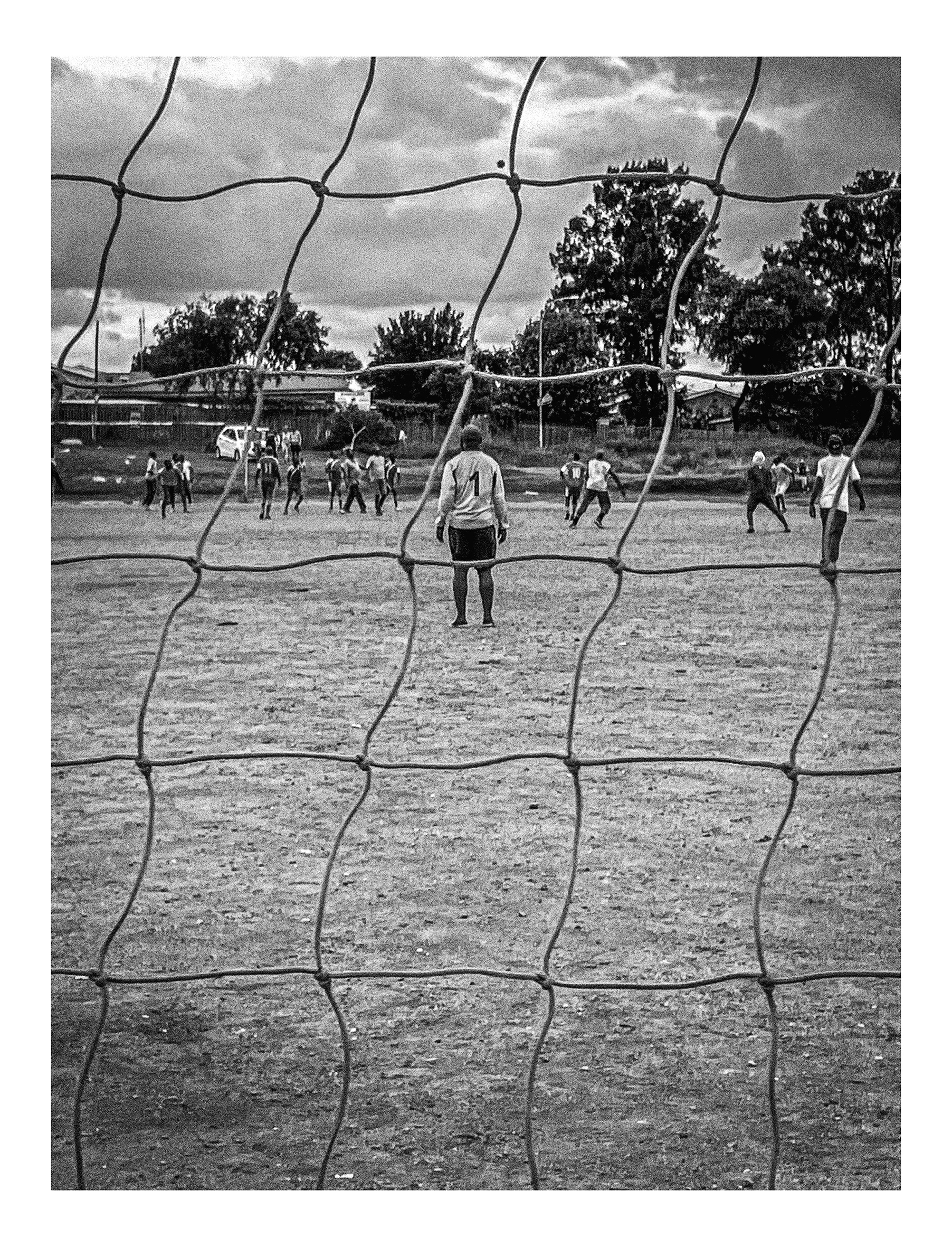 Andile Komasi's monochrome photograph 'Soccer Indaba' depicts a soccer player through a net.
