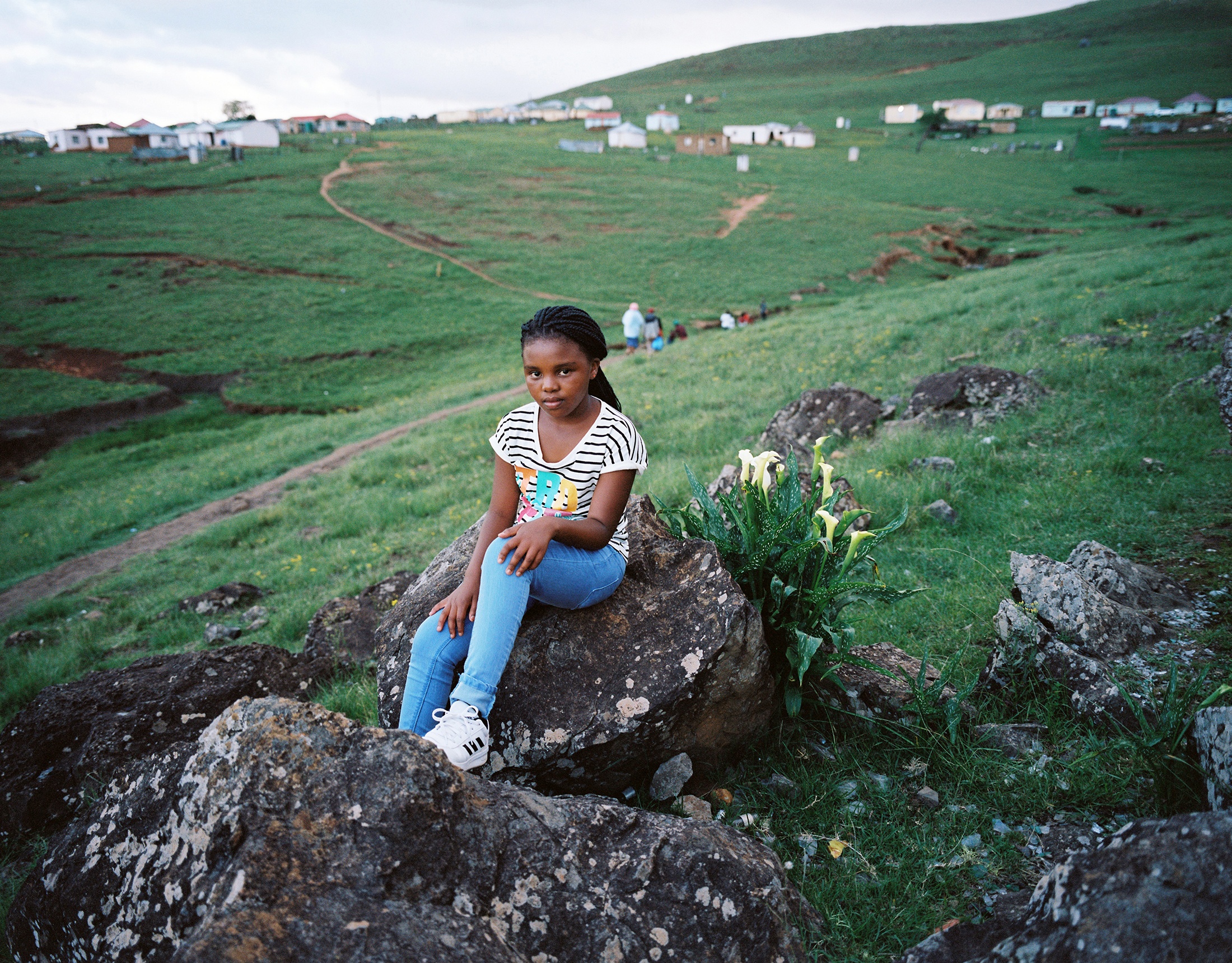 Lindokuhle Sobekwa's photograph 'Zenandi' shows a child sitting on an outcropping of rock on a grassy hill.
