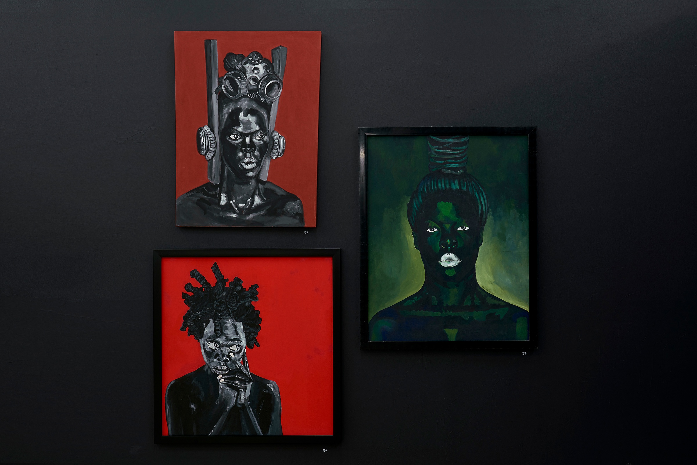 Installation photograph from the “Ikhono LaseNatali” exhibition in A4’s Gallery. On the left, Ncumisa Mcitwa’s acrylic painting “Somnyama Ngonyama, ‘Nambhla at Cassilbaus’” and Sphephelo Mnguni’s “Somnyama Ngonyama ‘Khwezi’” are mounted to a black gallery wall. On the right, Nomusa Musah Mtshali’s acrylic painting “Somnyama Ngonyama” is mounted on the wall.

