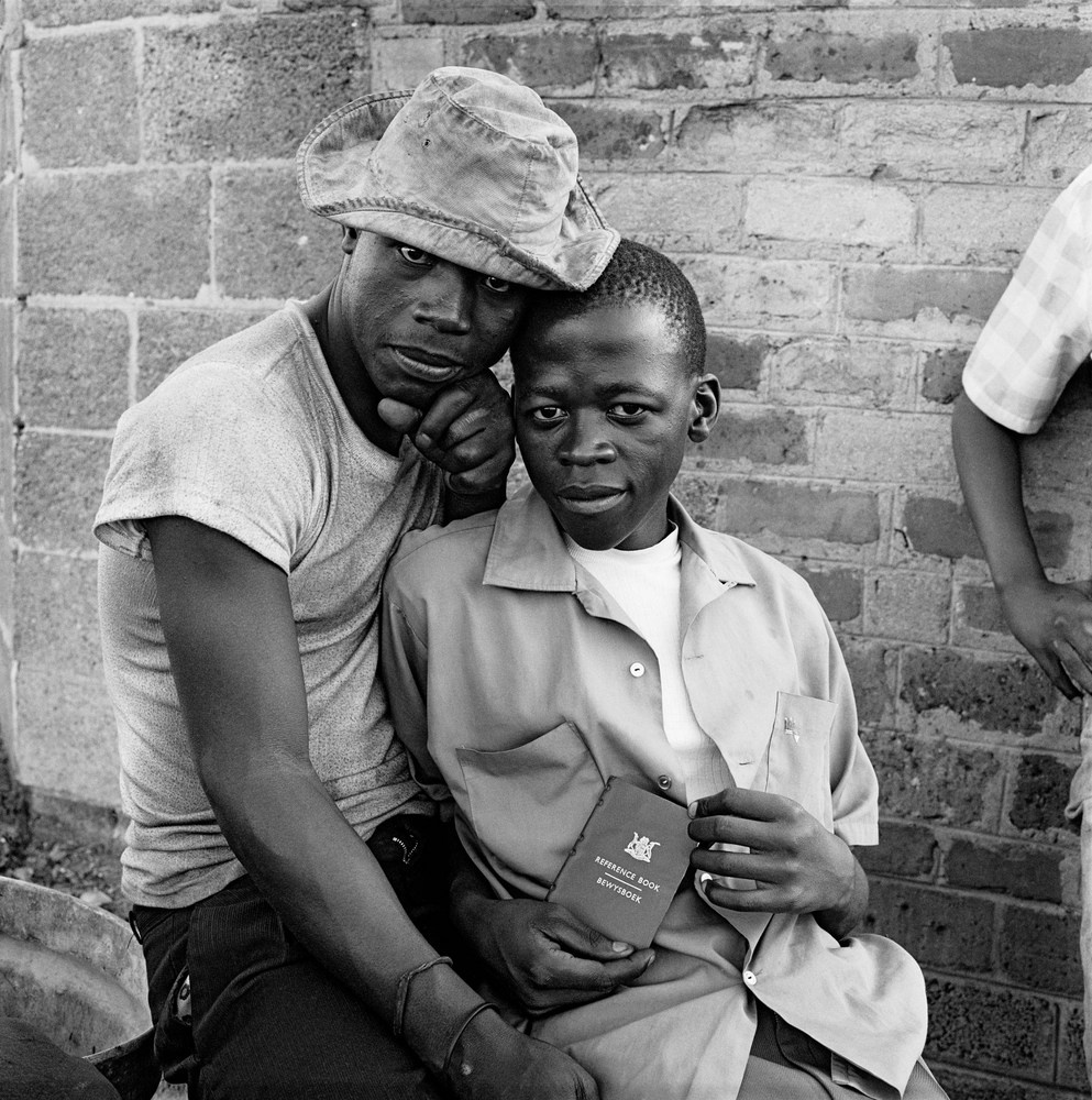 David Goldblatt's black-and-white photograph 'Young men with dompas (an identity document that every African had to carry), White City, Jabavu, Soweto' shows two seated men, one holding an identity document. 

