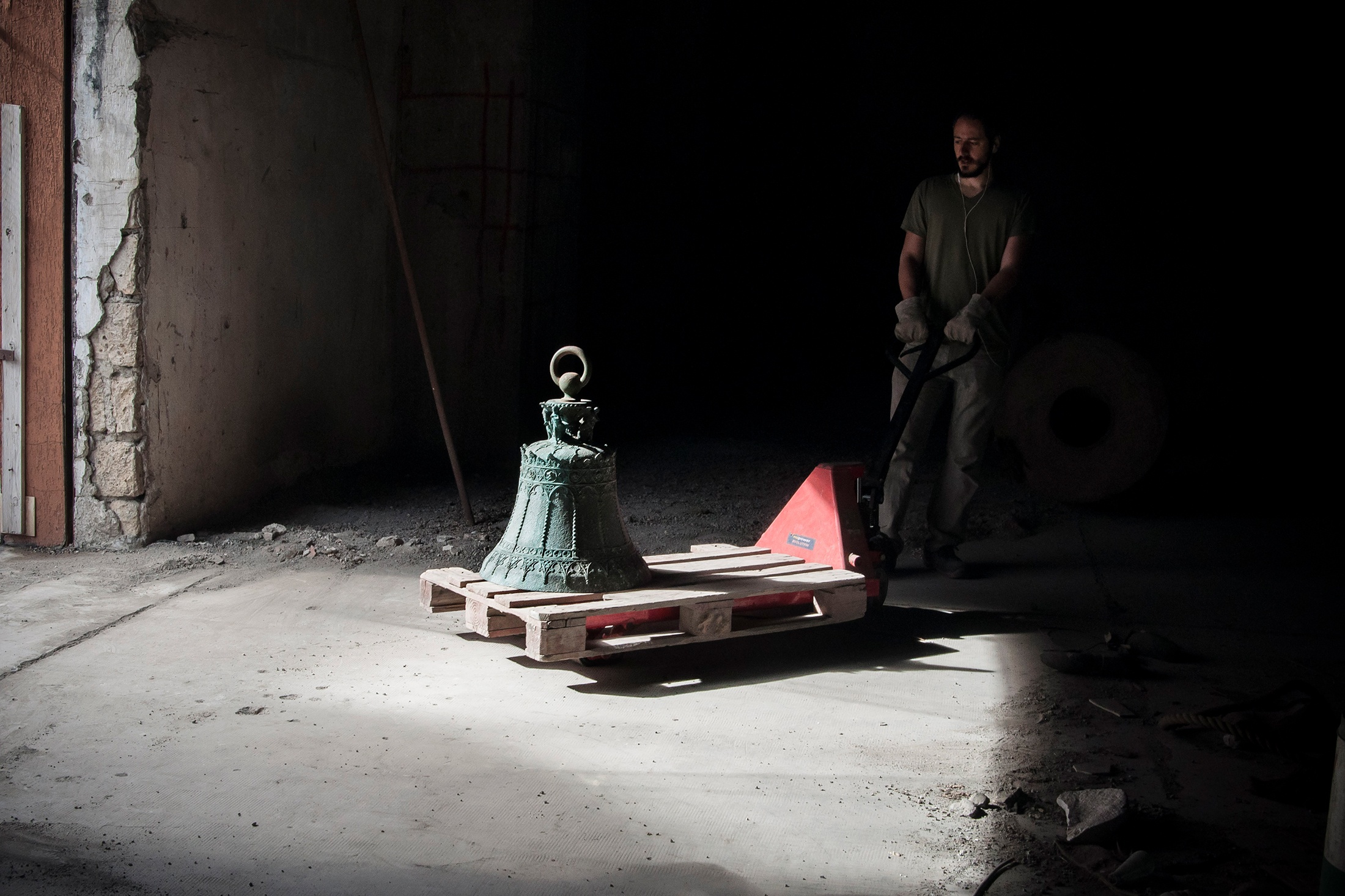 Still frame from ‘Sette Stagioni dello Spirito (Seven Seasons of the Spirit)’, a documentary about Gian Maria Tosatti’s series of installations of the same name. The image shows Tosatti moving a large ornate bell on a pallet jack.
