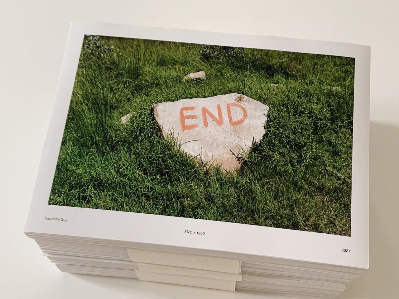 Photograph of a stack of Gabrielle Guy’s lithographic prints, titled ‘END x 1250’, itself a photograph of a rock laying on grass with the word ‘END’ painted on it.
