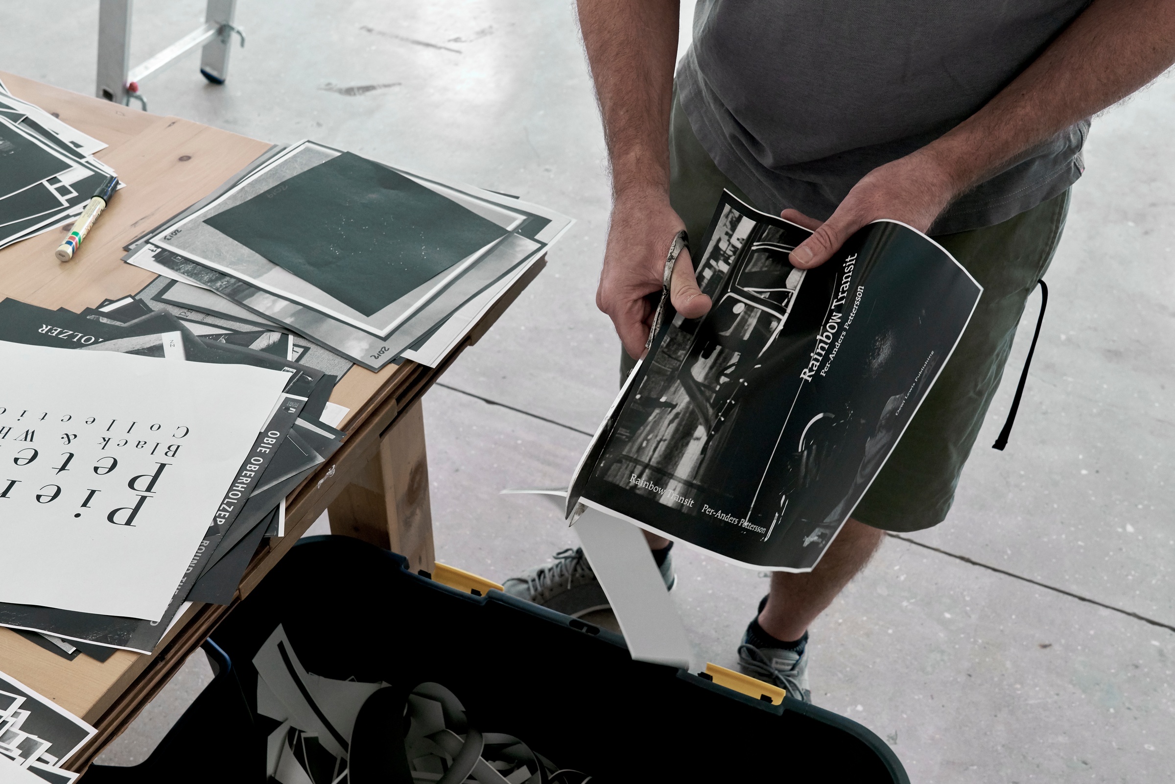 Process photograph from ‘Photobooks’, Sean O’Toole’s Course of Enquiry at A4. On the right, O’Toole trims the edges from a photocopy from his photobook collection. On the left, a wooden table laden with photocopies.
