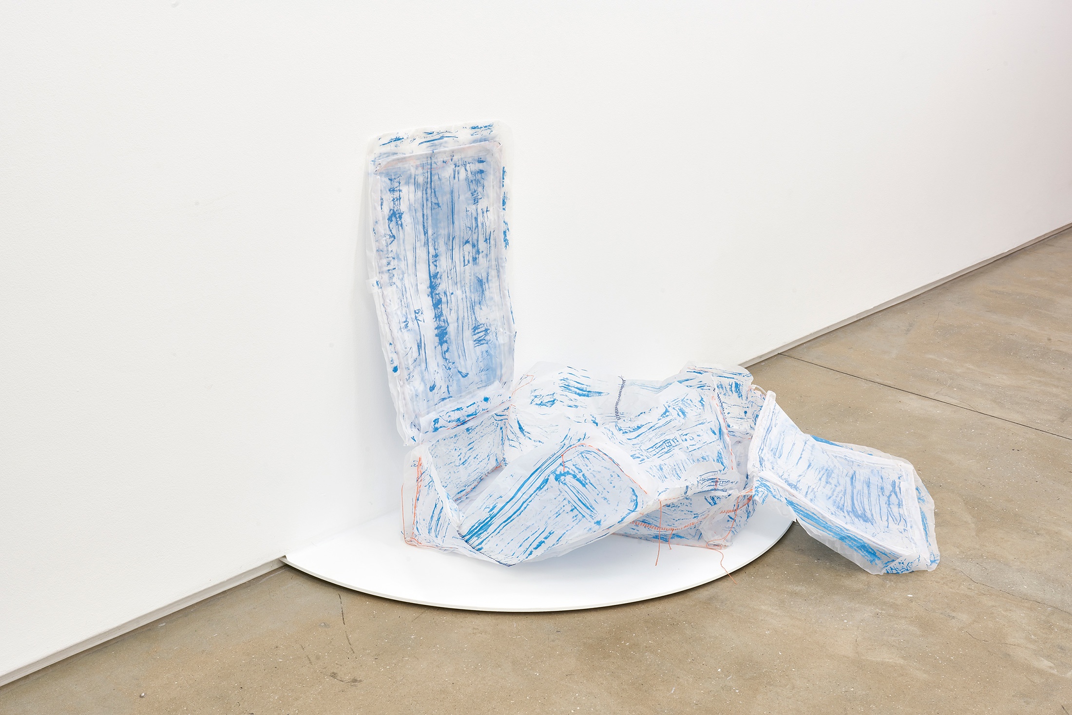 Installation photograph that shows Thato Makatu’s butcher-paper sculptural work ‘home is…' resting on a semi-circular white platform attached to the base of a white wall.
