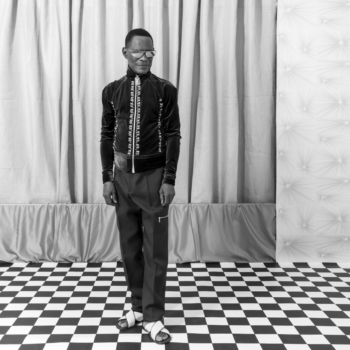 Samuel Fosso's monochrome photograph 'Autoportraits II (Fosso Fashion)' depicts an individual standing on a checkered floor.
