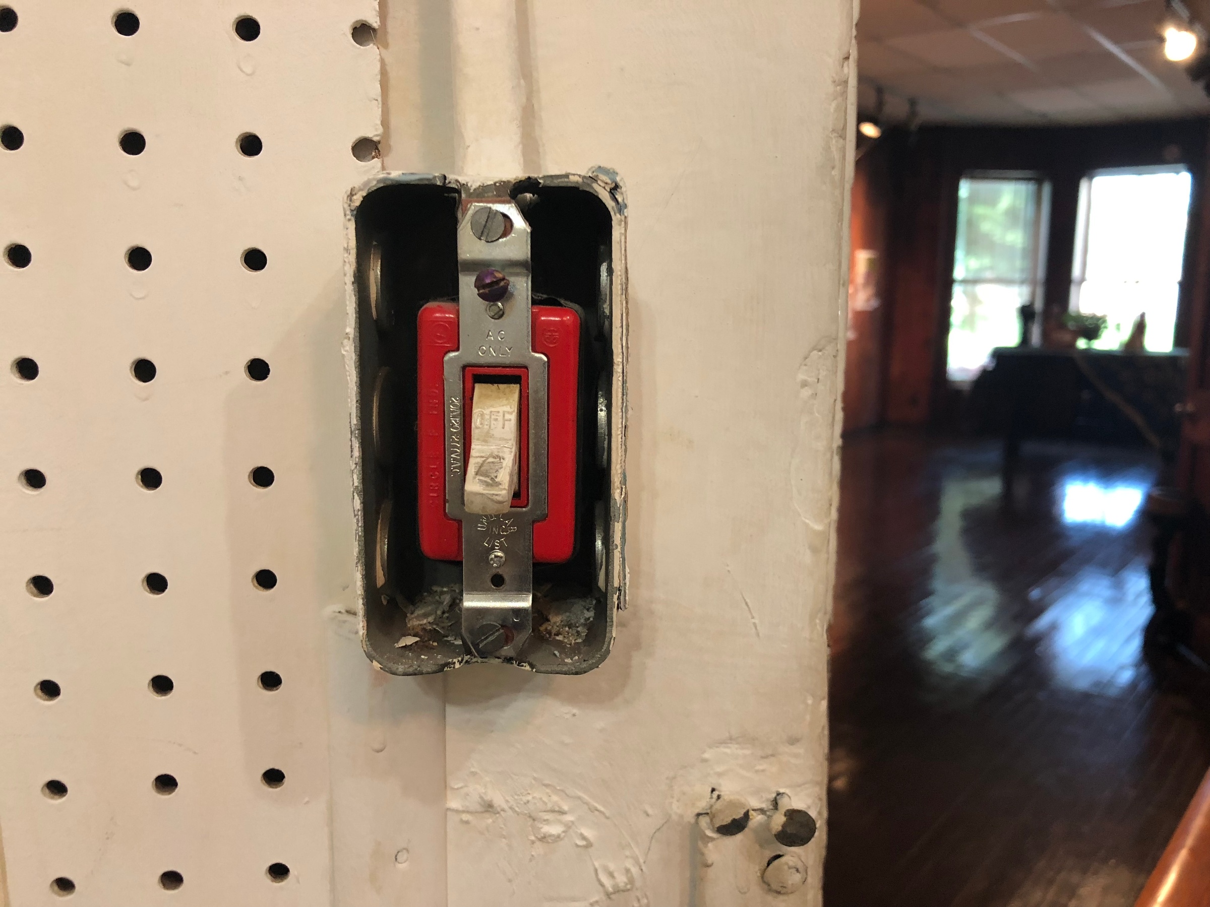 Ephemera from the offsite event ‘On Curating: Institutions and their Social Fabrics’ at the Art Institute of Chicago. An electric light switch without a cover sits on a perforated white wall.
